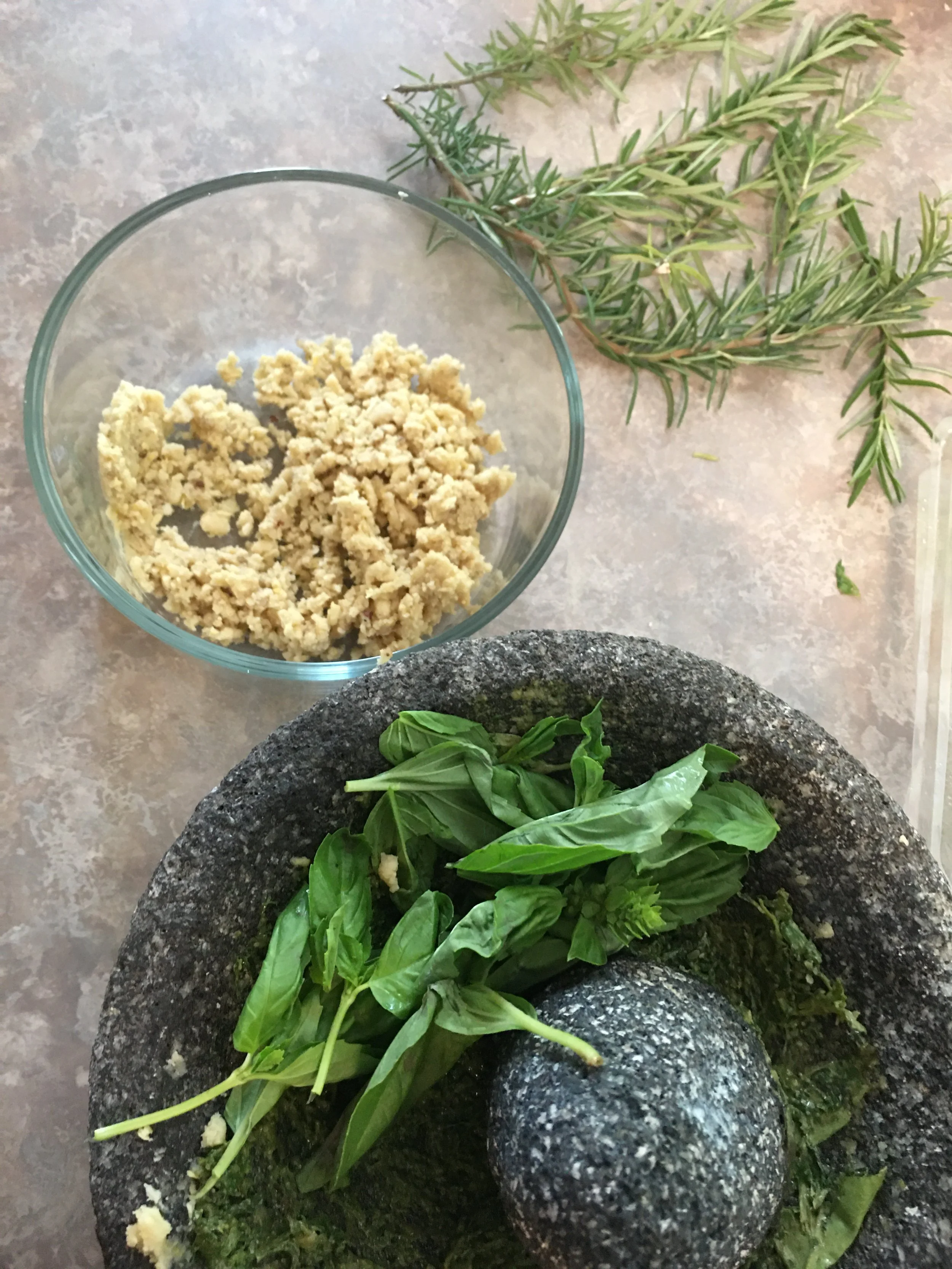 Fresh basil leaves on a black granite mortar and pestle with chopped garlic, a bowl of crushed garlic, and sprigs of fresh thyme on a kitchen countertop at The Oak Room in Chickasaw Springs.