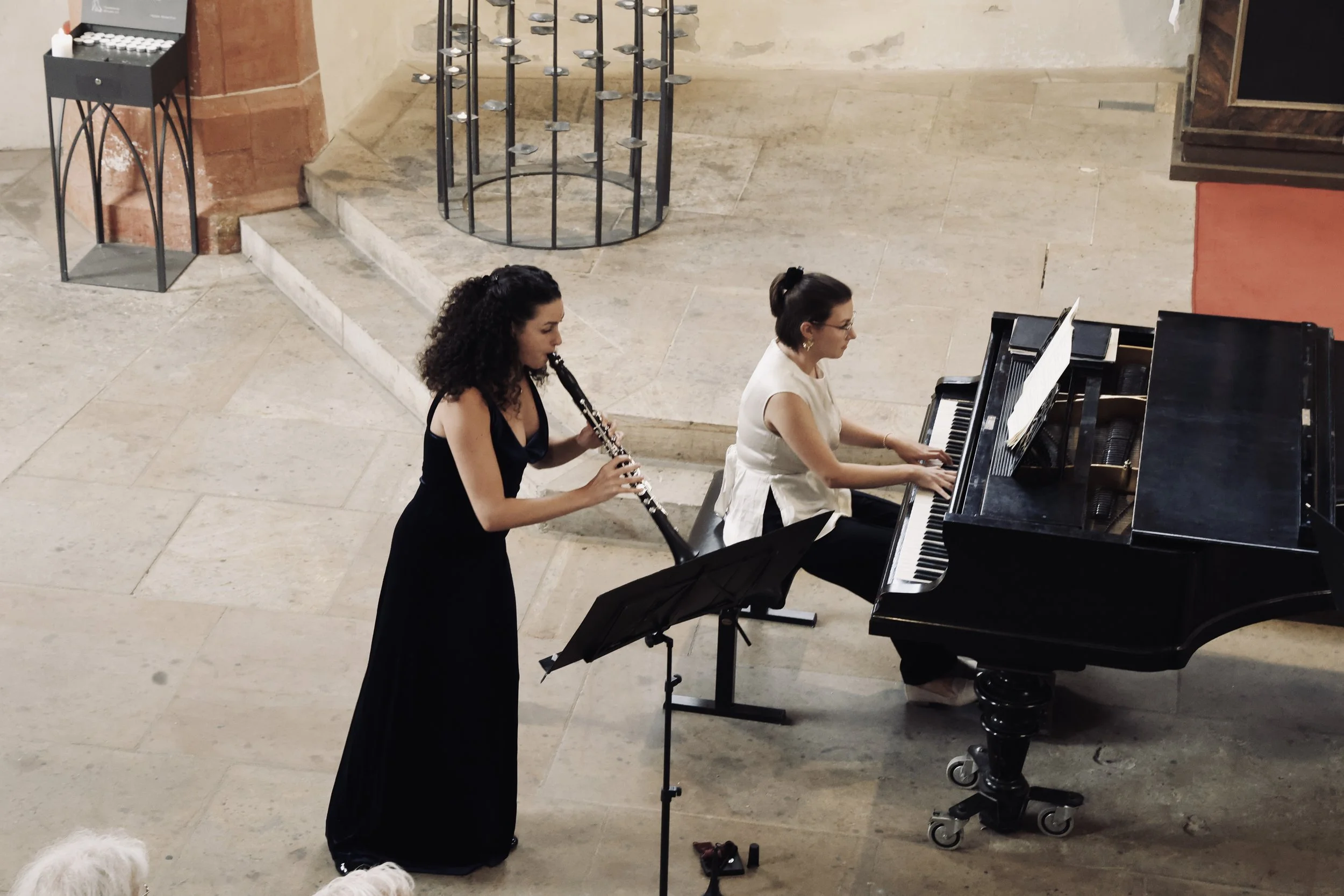 Zwei Frauen spielen gemeinsam Klavier und Klarinette in einem Raum mit Steinboden und ungleichmäßigen Wänden.