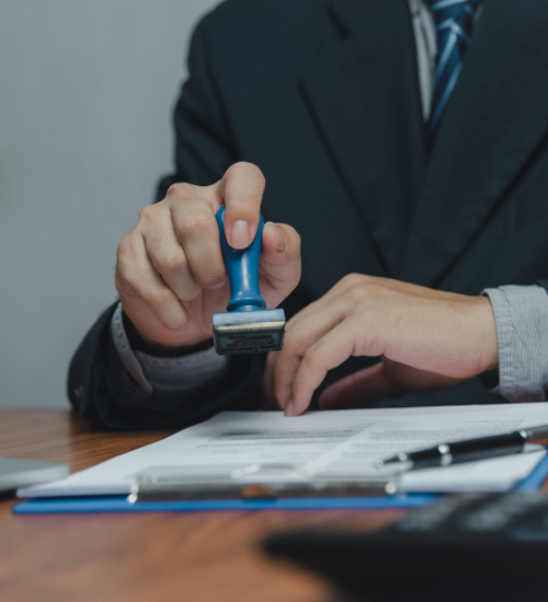 Persona con traje sellando un documento con un sello de respaldo en un escritorio.