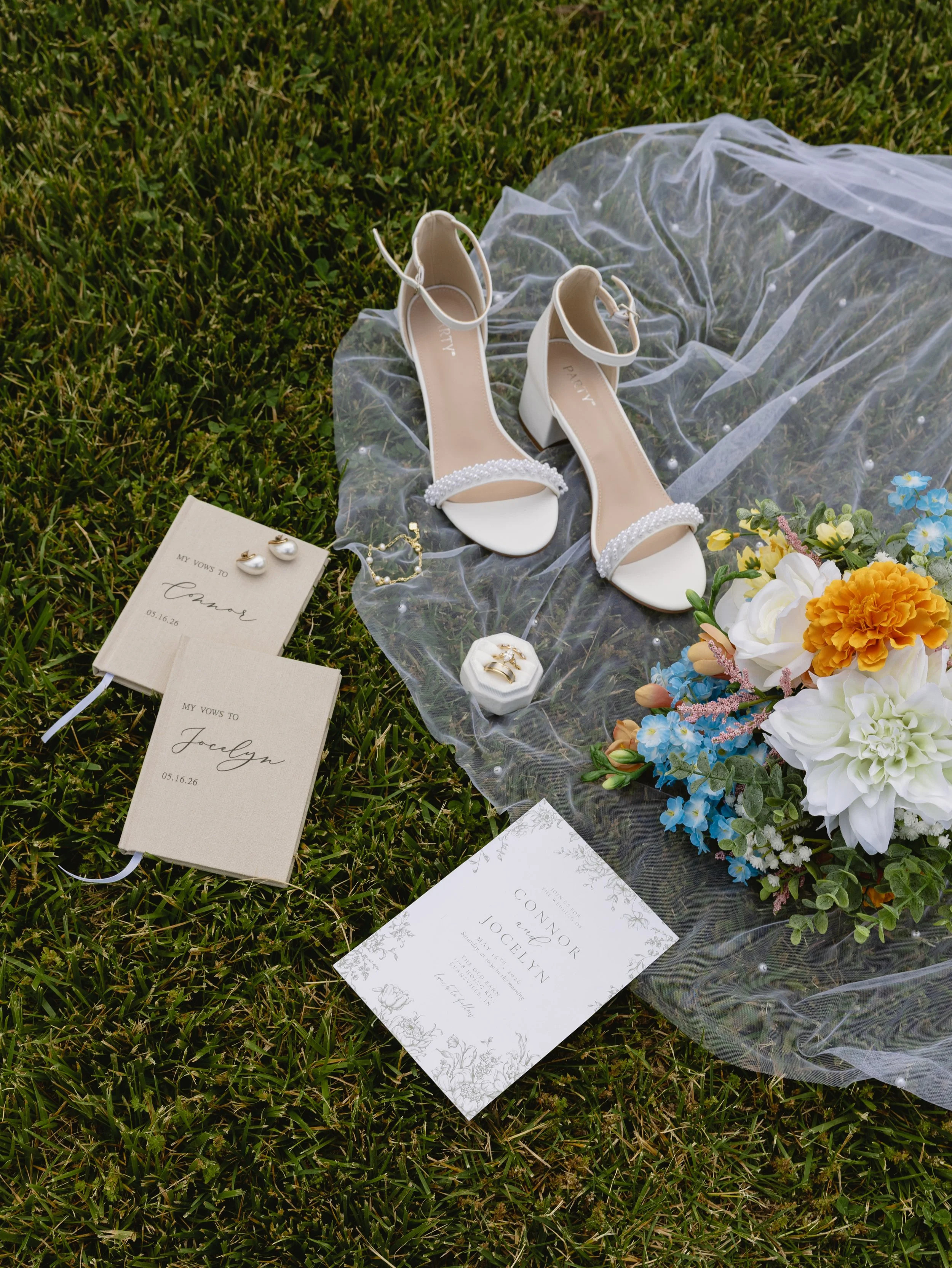 White wedding shoes, bridal bouquet, and wedding invitation on grass