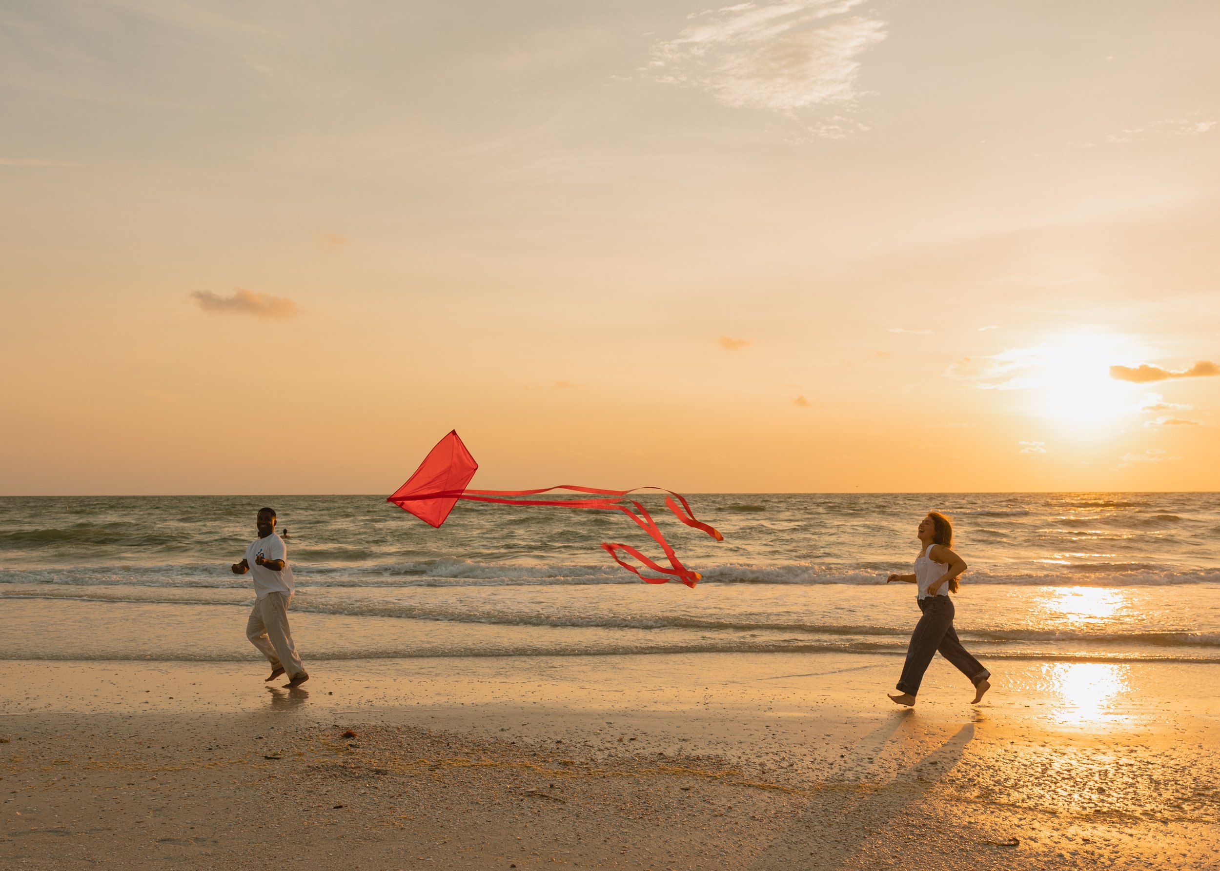 Two people flying a red kite on the beach during sunset.