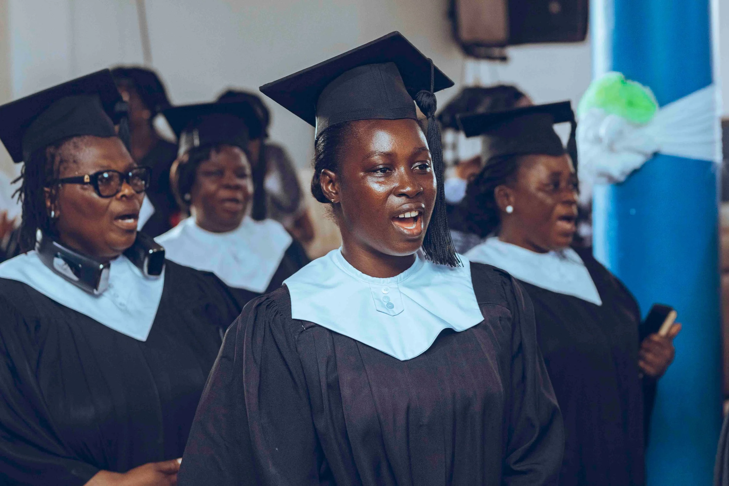 Group of diverse women wearing graduation caps and gowns during a graduation ceremony.
