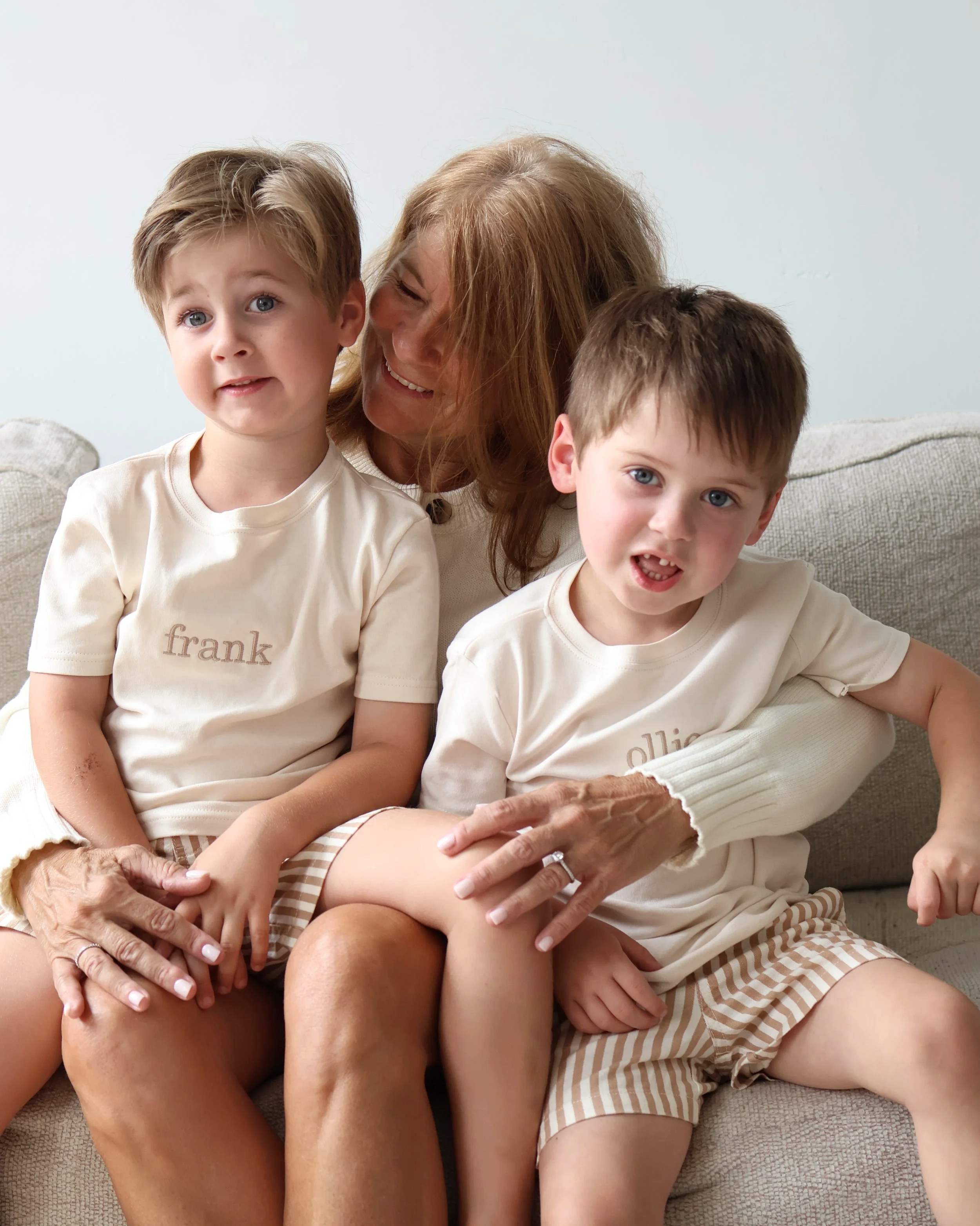 Two young boys wearing personalized Frank & Ollie name T-shirts, sitting together with their grandmother.