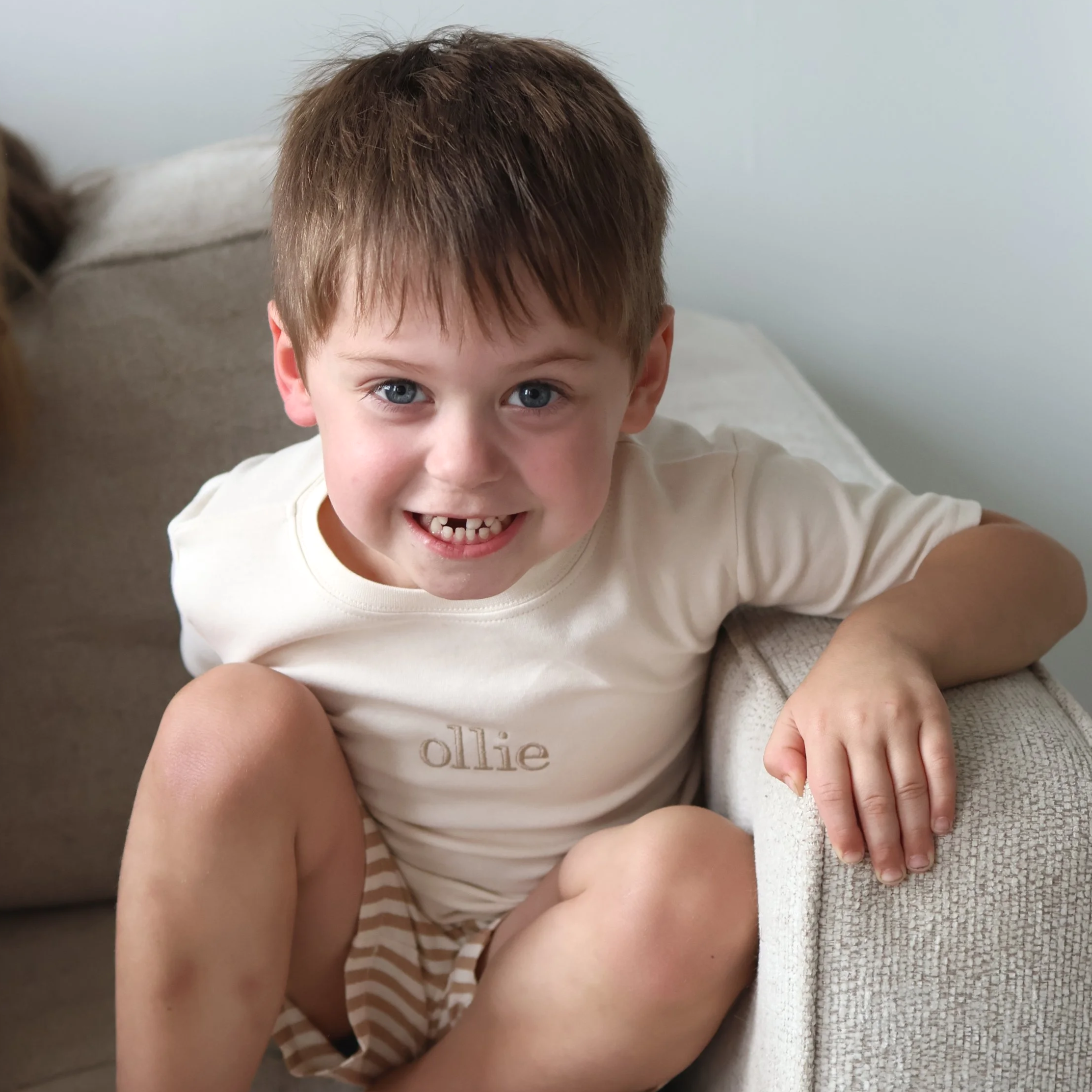 Young boy relaxing in a personalized Frank & Ollie name T-shirt in a cozy home setting.