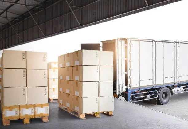 Boxes stacked on pallets next to a cargo truck in a warehouse or loading dock.