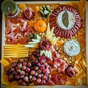 An assortment of food items including grapes, sliced meats, cheeses, fruit, green olives, and crackers.