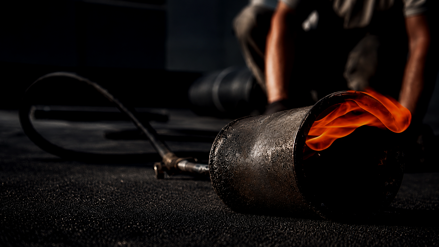 Un travailleur utilisant un chalumeau pour couper un tuyau en métal enflammé, avec un fond sombre et un sol noir.