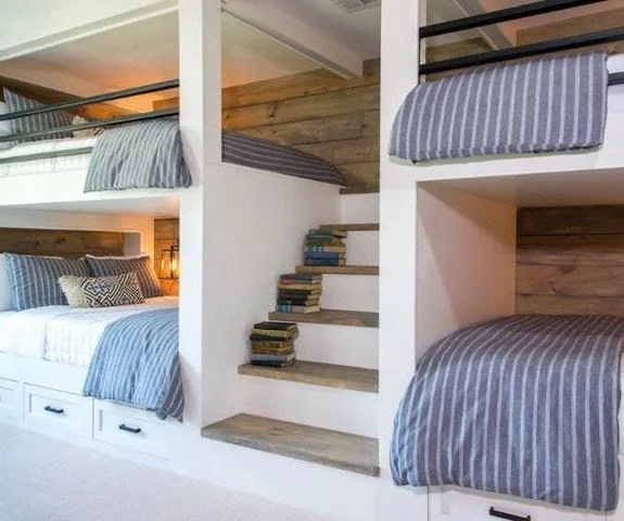 A bedroom with two bunk beds, each with striped bedding, and a staircase with books on the steps.