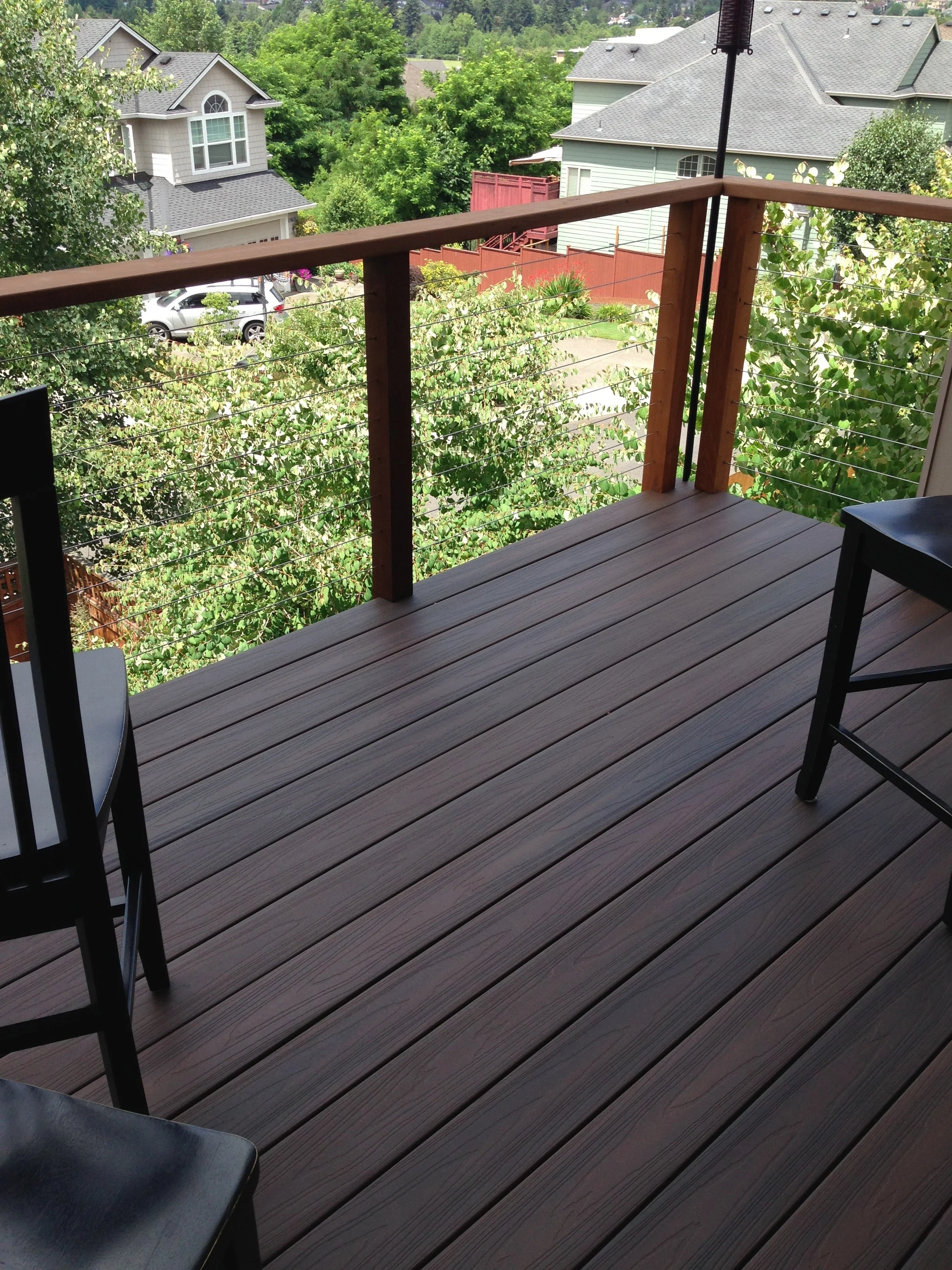 View from a balcony showing neighboring houses, trees, and a street with parked cars. Composite deck with cable rail.