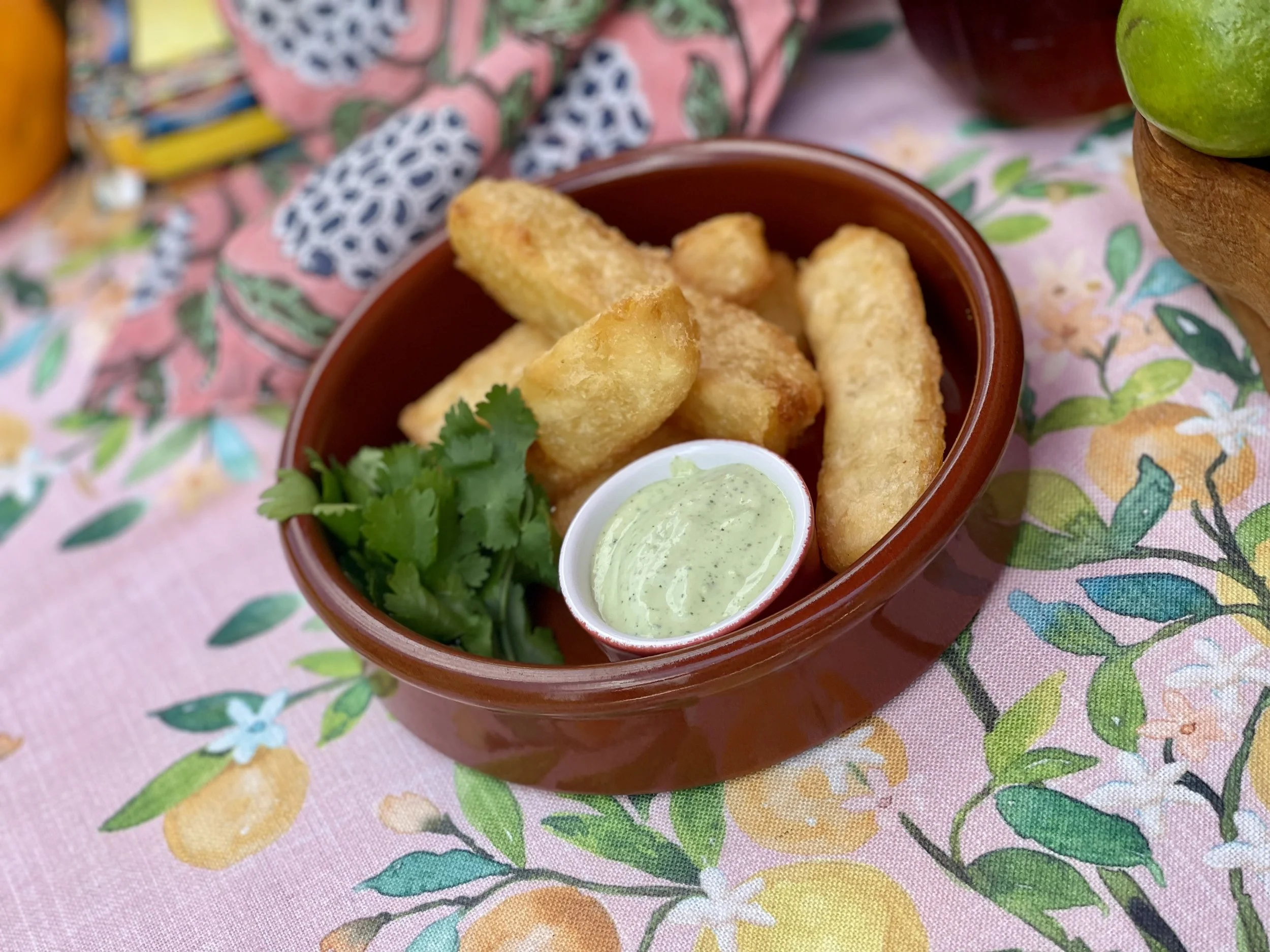 Bowl of fried fish with tartar sauce, garnished with cilantro and served on floral tablecloth.