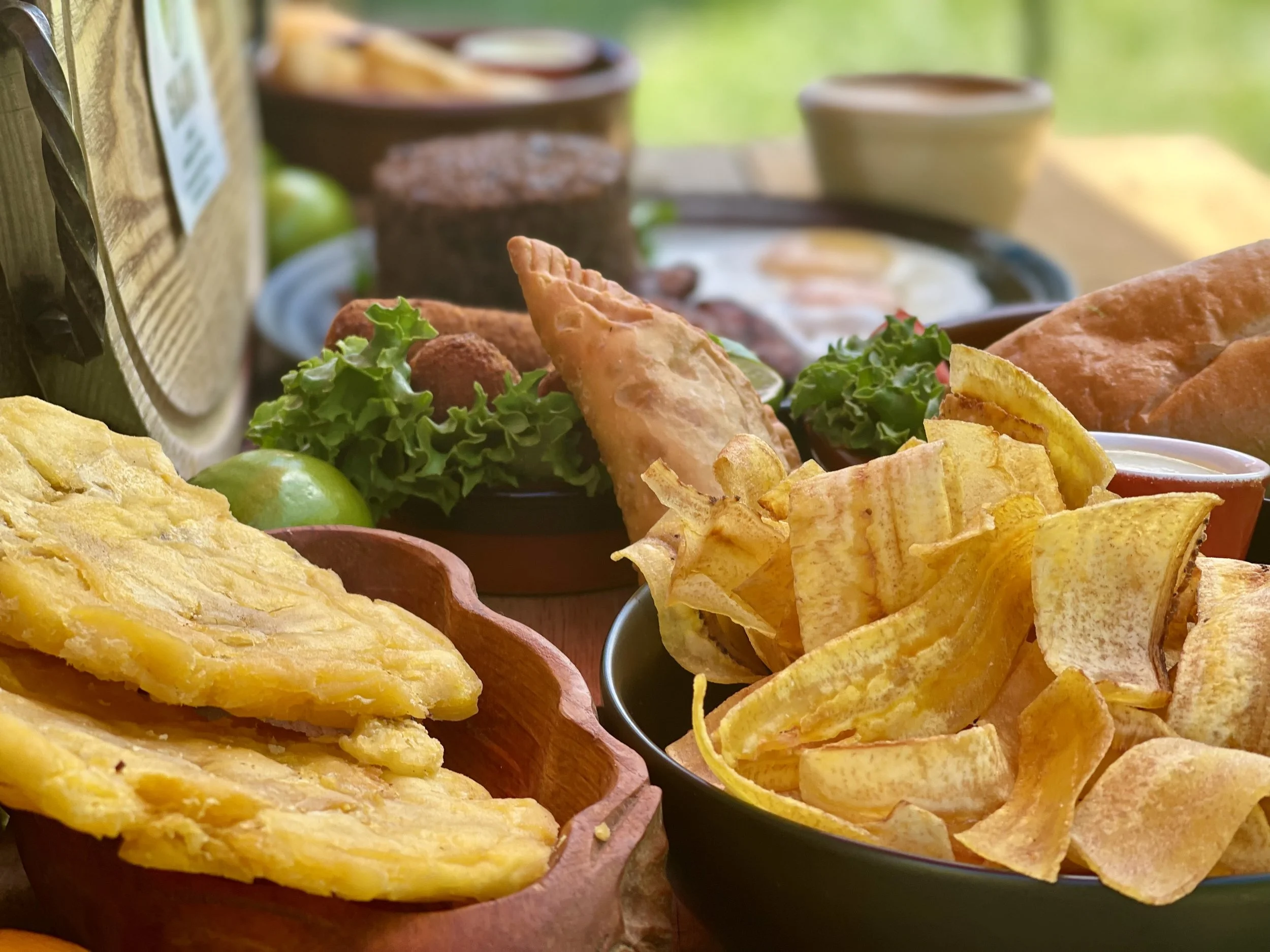 Assorted Mexican food dishes including chips, salsa, dips, and a plate of skewers on a table outdoors.