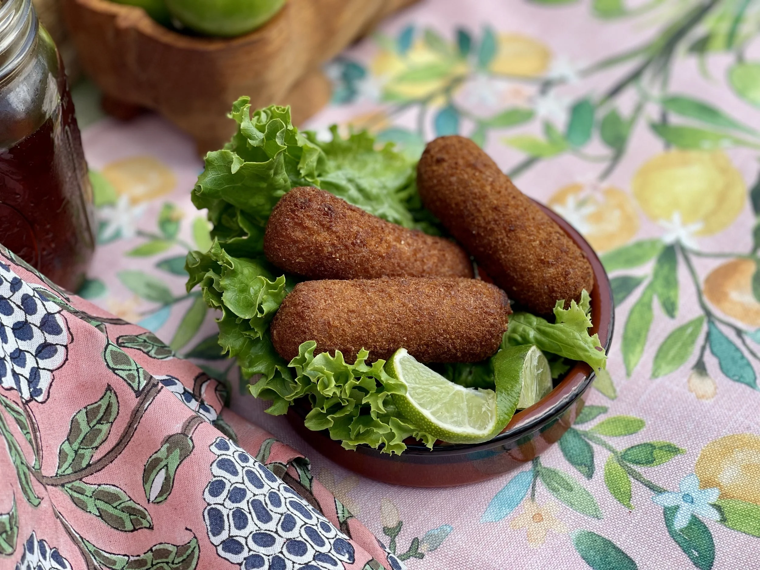Fried croquettes served on a plate with lettuce and lemon wedge, on a colorful tablecloth.