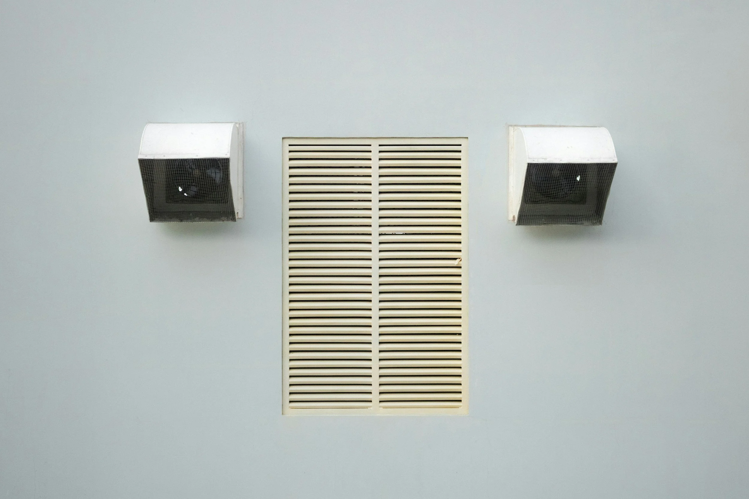 Ceiling with two white square speaker vents and a rectangular air vent in the center, all mounted on a light gray ceiling.