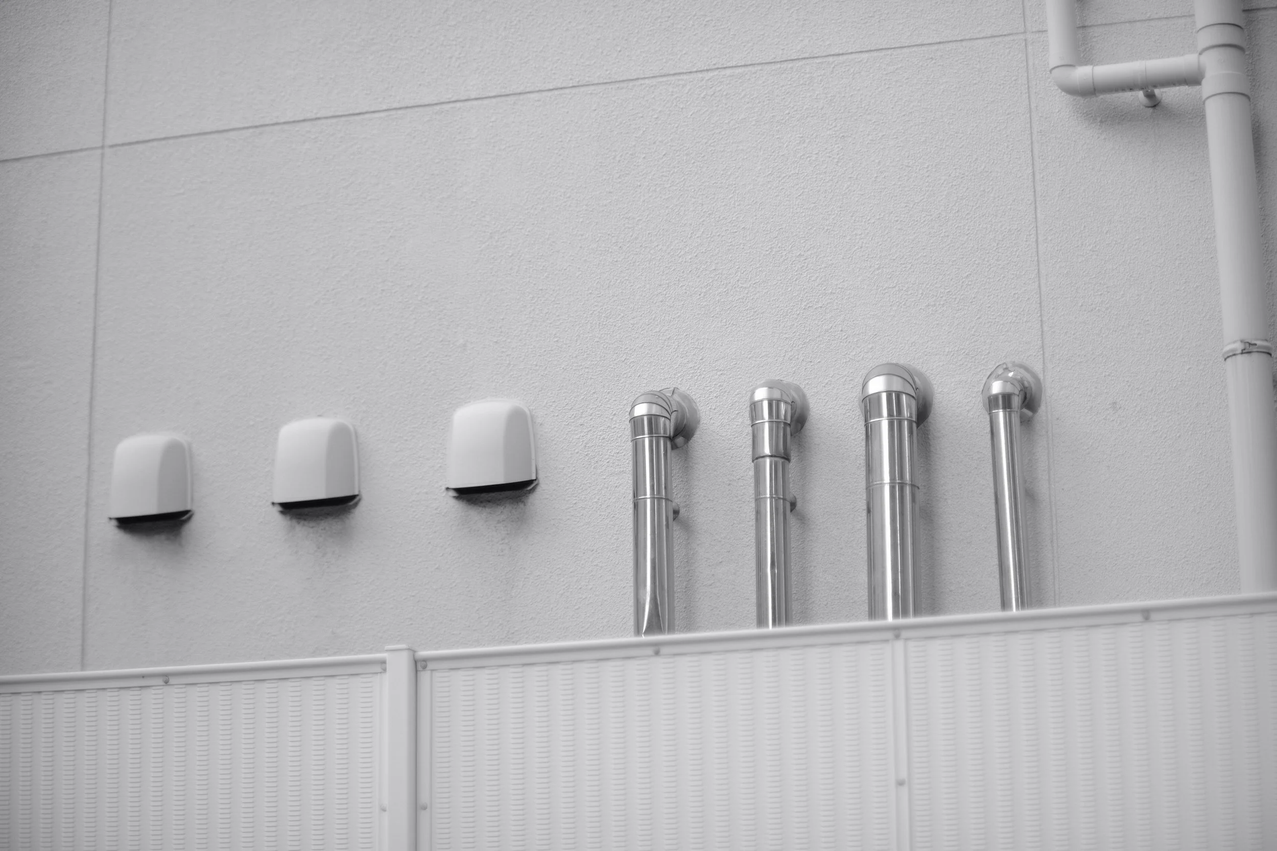 Wall with six white plastic caps and five metallic pipes on a textured light gray wall.