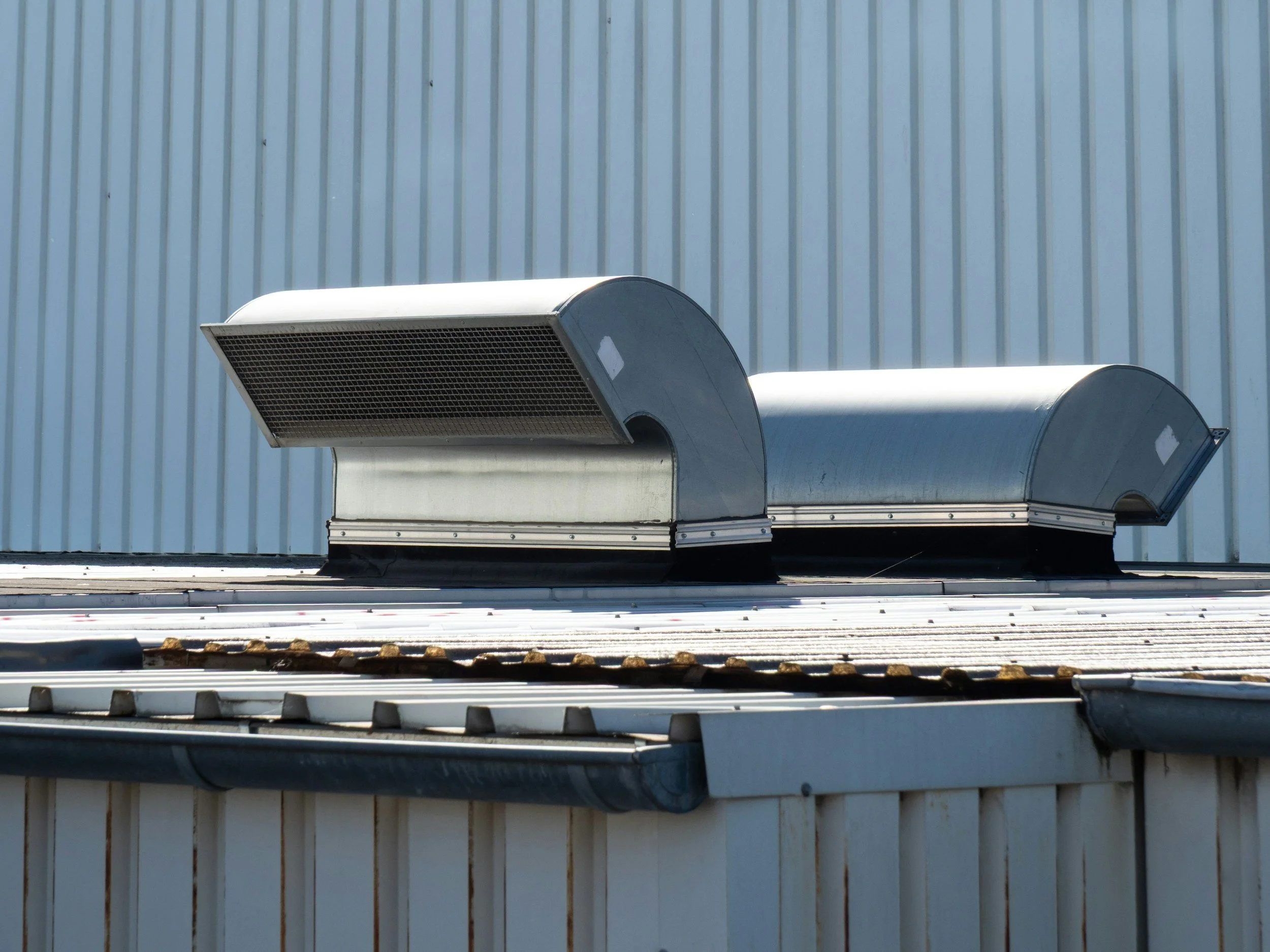 Close-up of industrial ventilation ducts mounted on the side of a building with vertical metal siding.