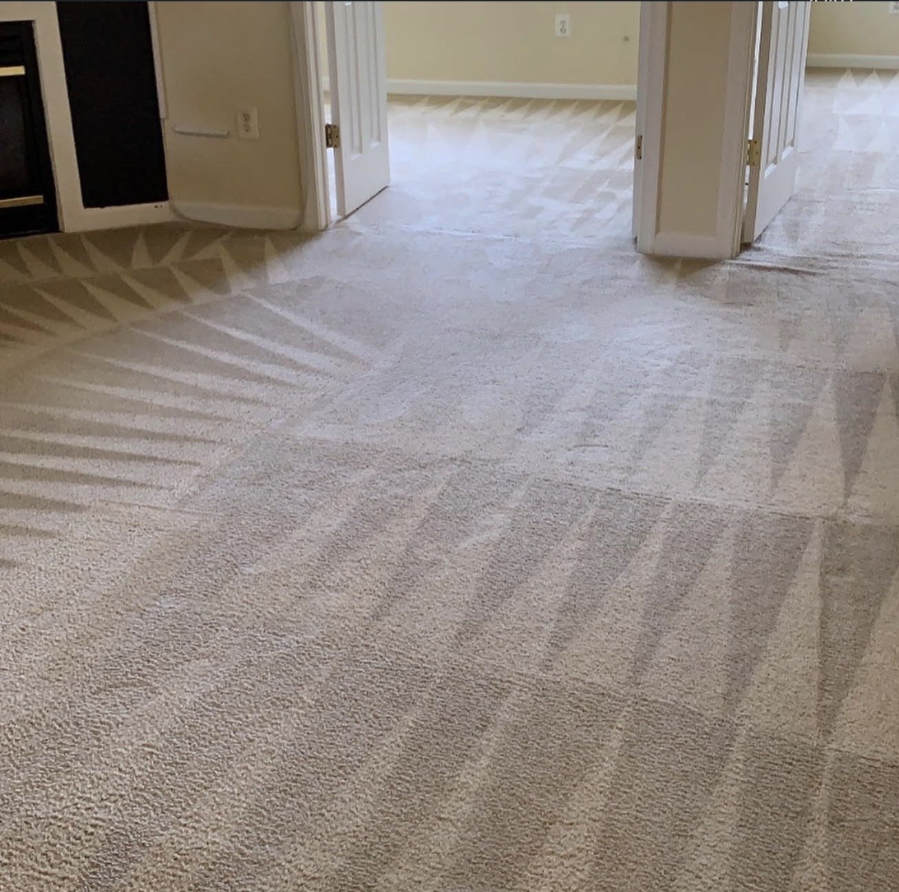 Carpeted floor with vacuum cleaner lines in a residential room, showing doorways and part of a bathroom or kitchen area.