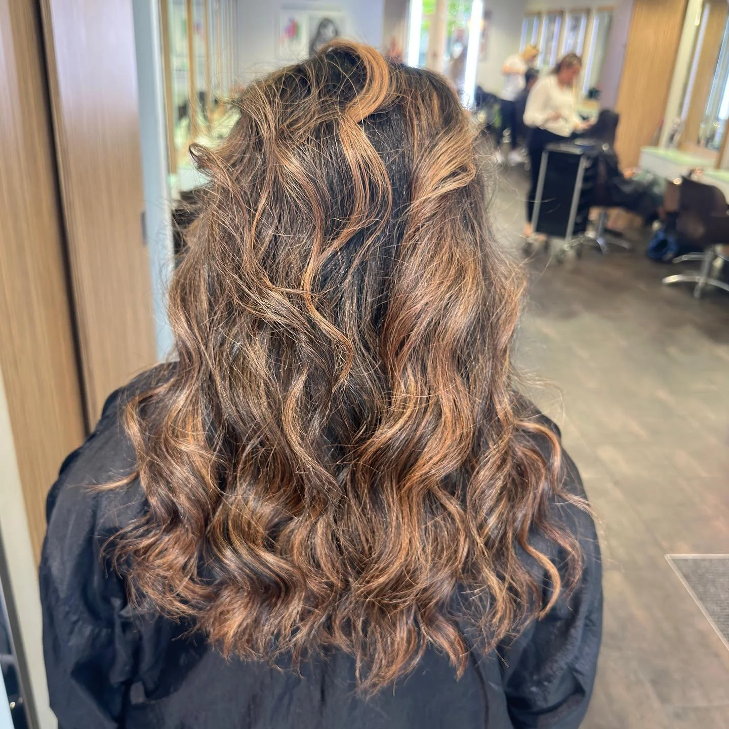 Woman with curly hair in a salon with other clients and hairstylists in the background.