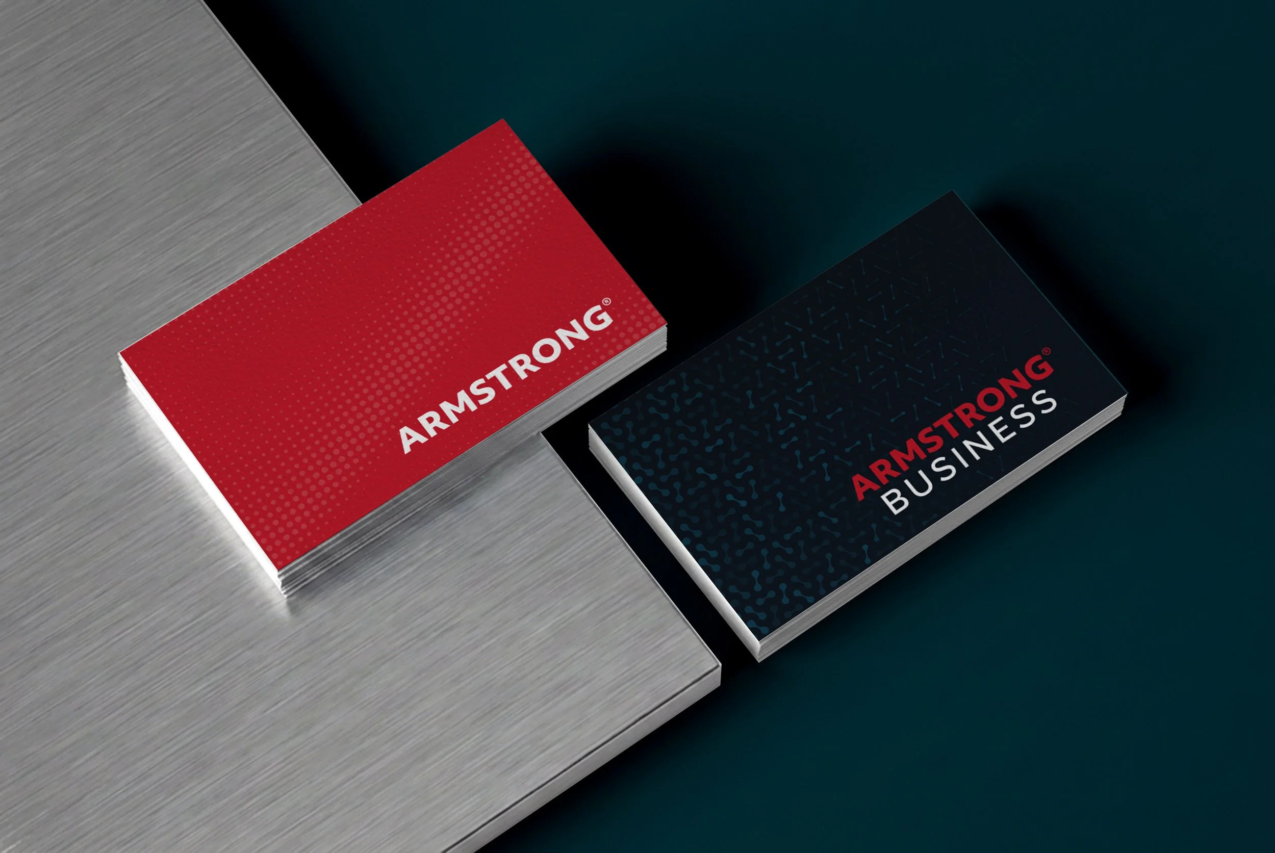 Close-up of business cards on a table, one red with white text 'ARMSTRONG' and one black with red and white text 'ARMSTRONG BUSINESS'.