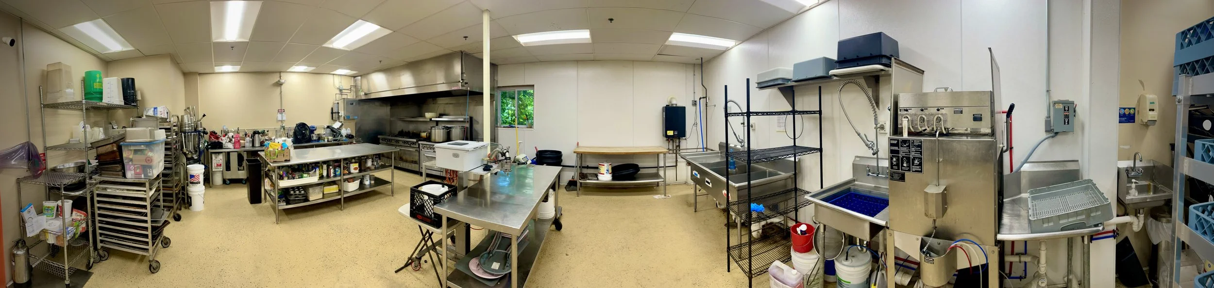 Commercial kitchen with stainless steel appliances, sinks, shelving, and cleaning supplies.