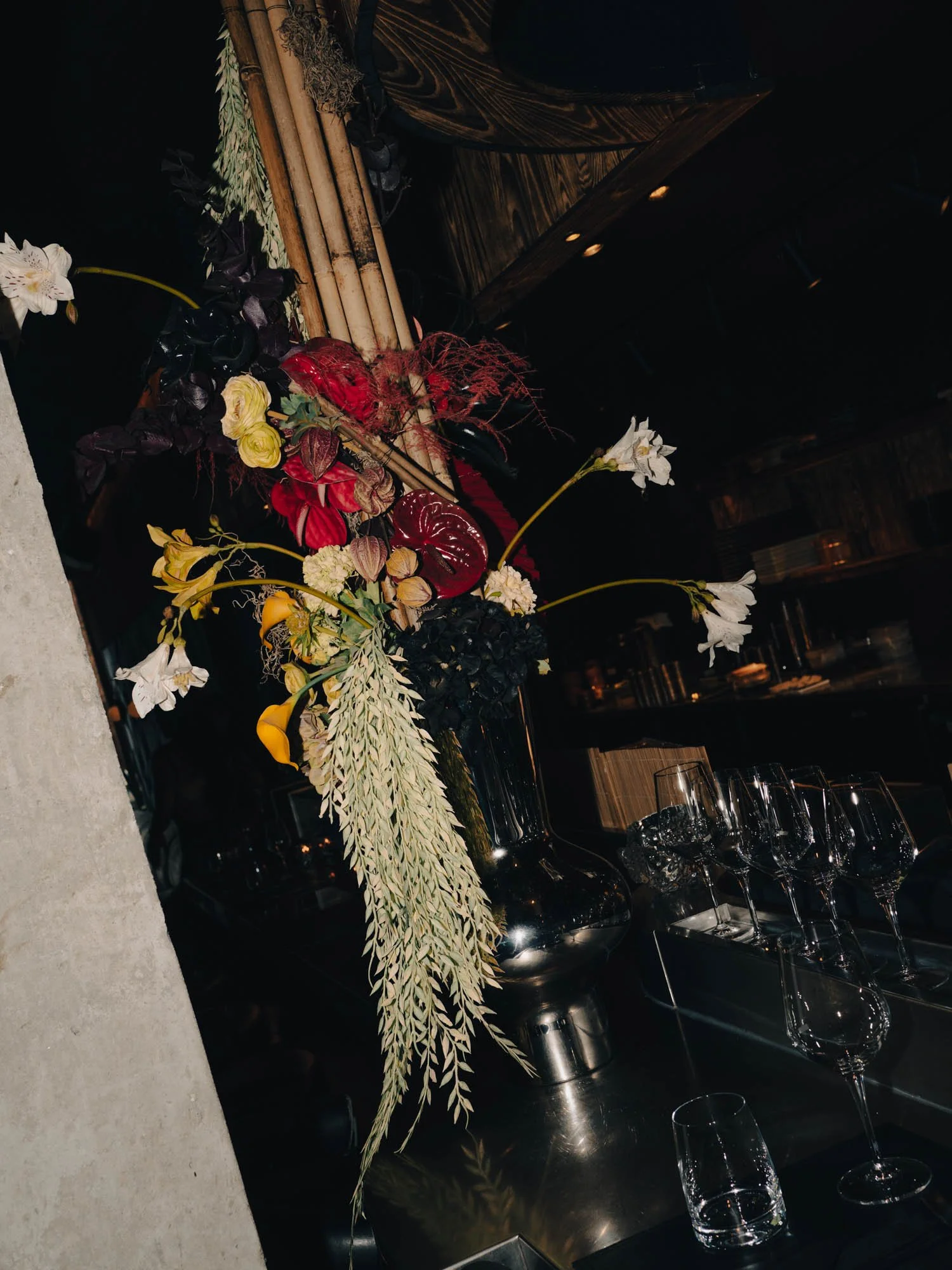 RYU Flowers. Elegant flower arrangement with white, yellow, red, and dark purple flowers, along with greenery, displayed on a black surface in a dimly lit setting.