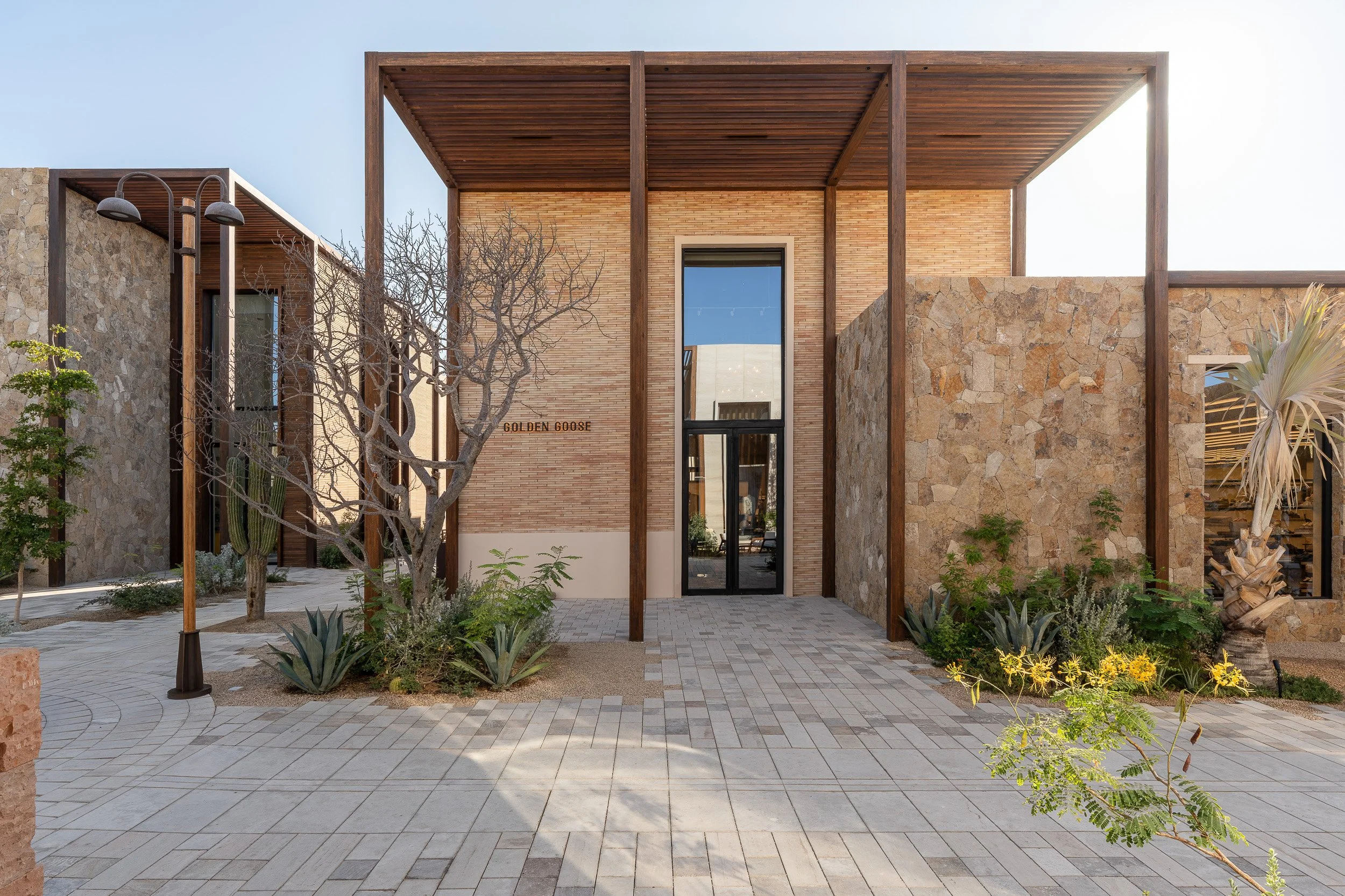 Modern building with stone and wood exterior, large glass door, and a courtyard with potted plants and trees.