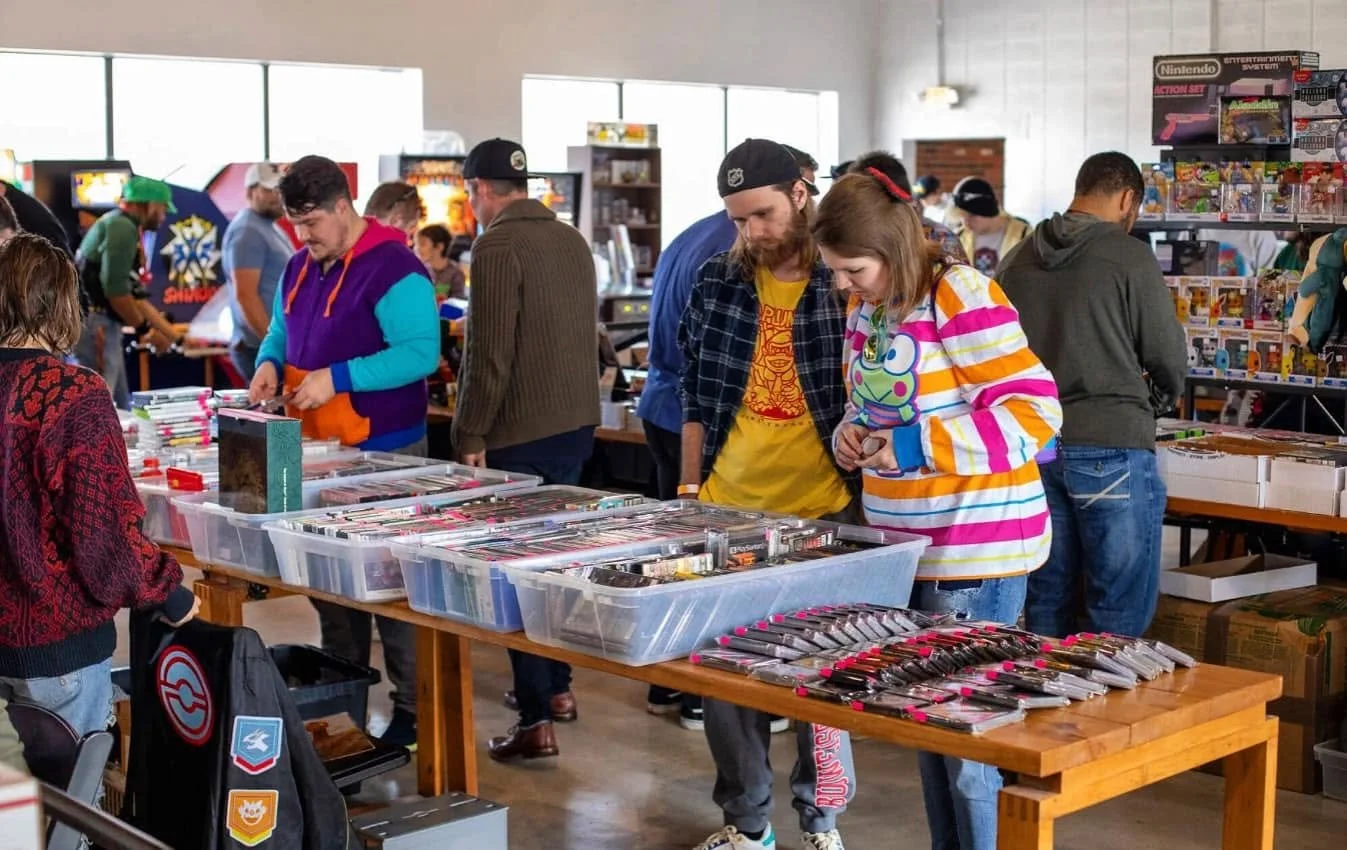 People browsing through tables filled with vintage video game and toy merchandise at a store or convention.