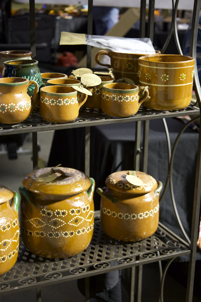 Collection of handmade glazed ceramic pots and mugs with floral and geometric painted designs displayed on a metal shelf.