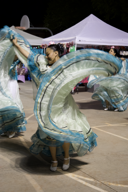 Woman performing a traditional dance in a flowing blue and green dress at an outdoor event with tents in the background.