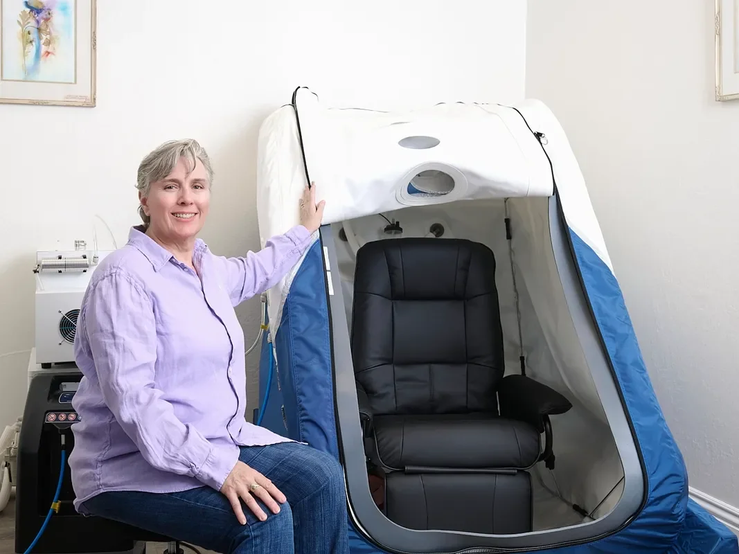 Sorena Linton seated beside the open soft-sided hyperbaric chamber at SoRay Hyperbarics.