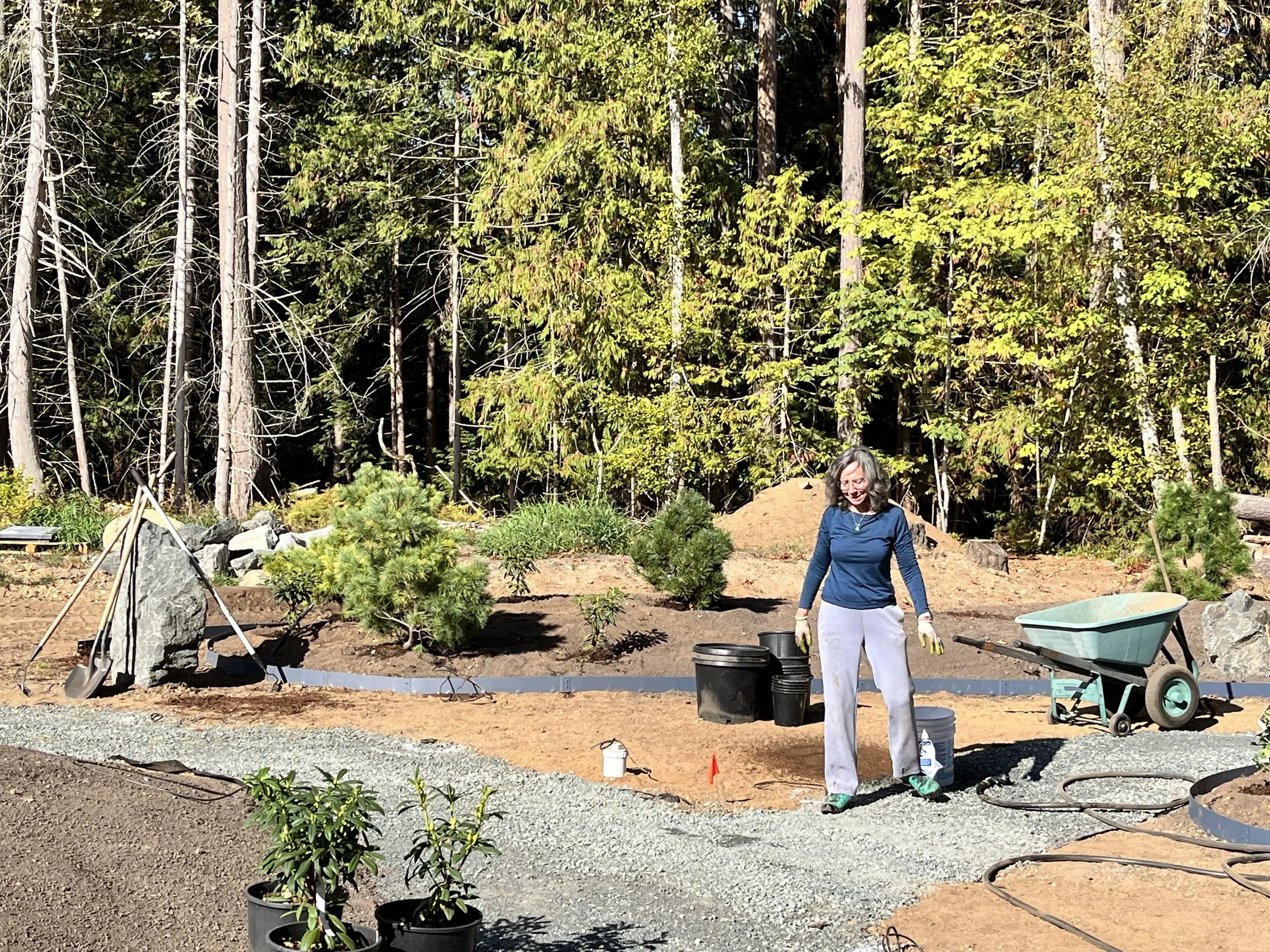 Woman building a Japanese garden with shovels, plants, rocks, soil, and a wheelbarrow. Qualicum Beach, British Columbia.
