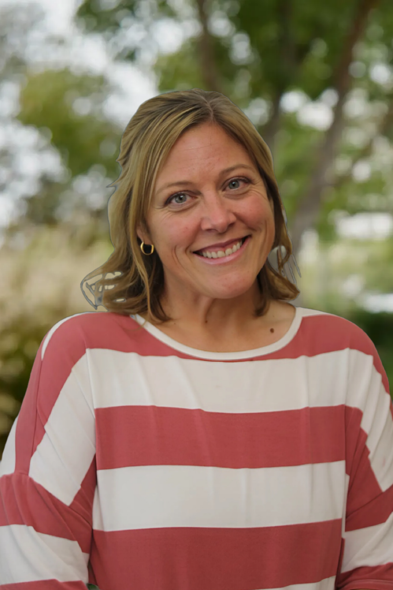 A smiling woman with shoulder-length wavy blonde hair, blue eyes, and fair skin, wearing a red and white striped long-sleeve shirt, standing outdoors with blurred greenery in the background.