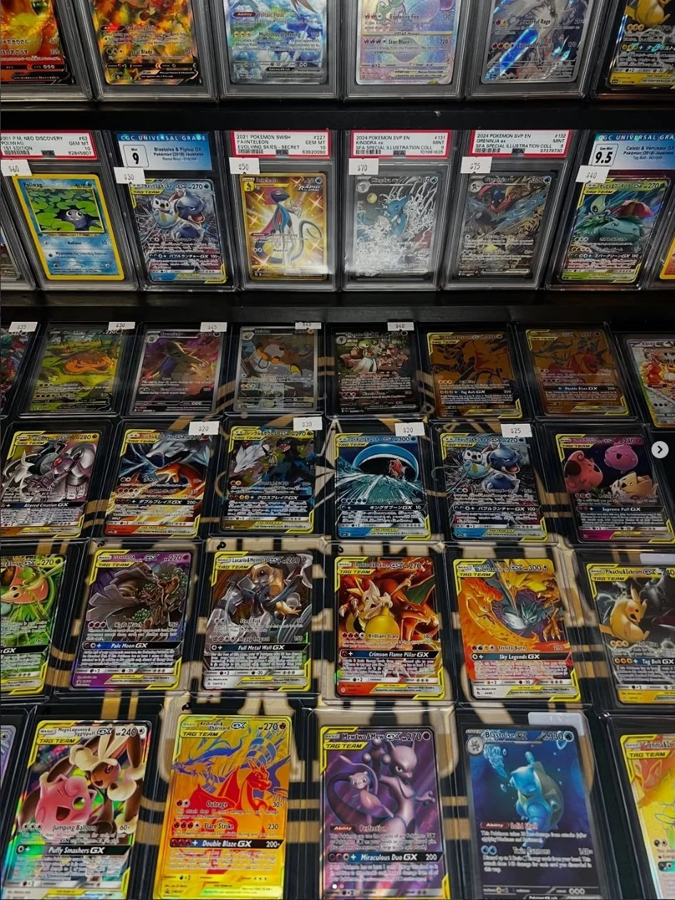 Display of Pokémon trading cards in plastic sleeves, arranged in rows and columns, with some cards labeled with prices.