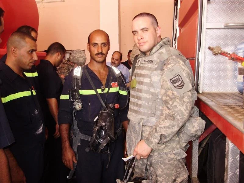 Group of firefighters and a soldier inside a fire station, some in uniform and equipment.