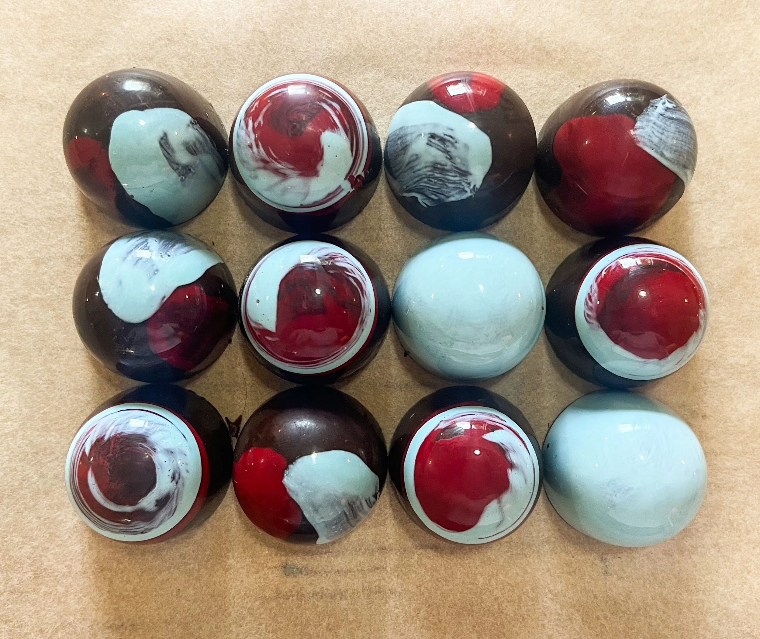 A collection of rolled marbles with swirled patterns in red, white, black, and blue colors arranged on a beige surface.