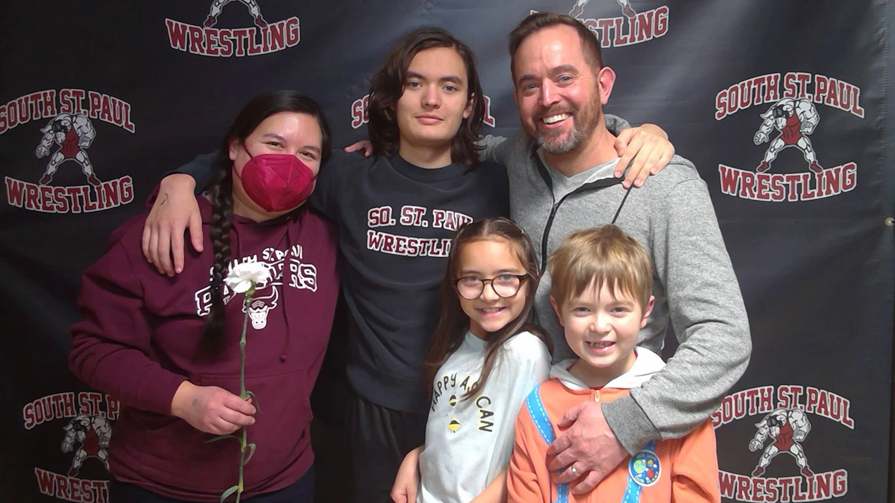 The five members of the Humann family posing in front of a South St. Paul Wrestling banner.