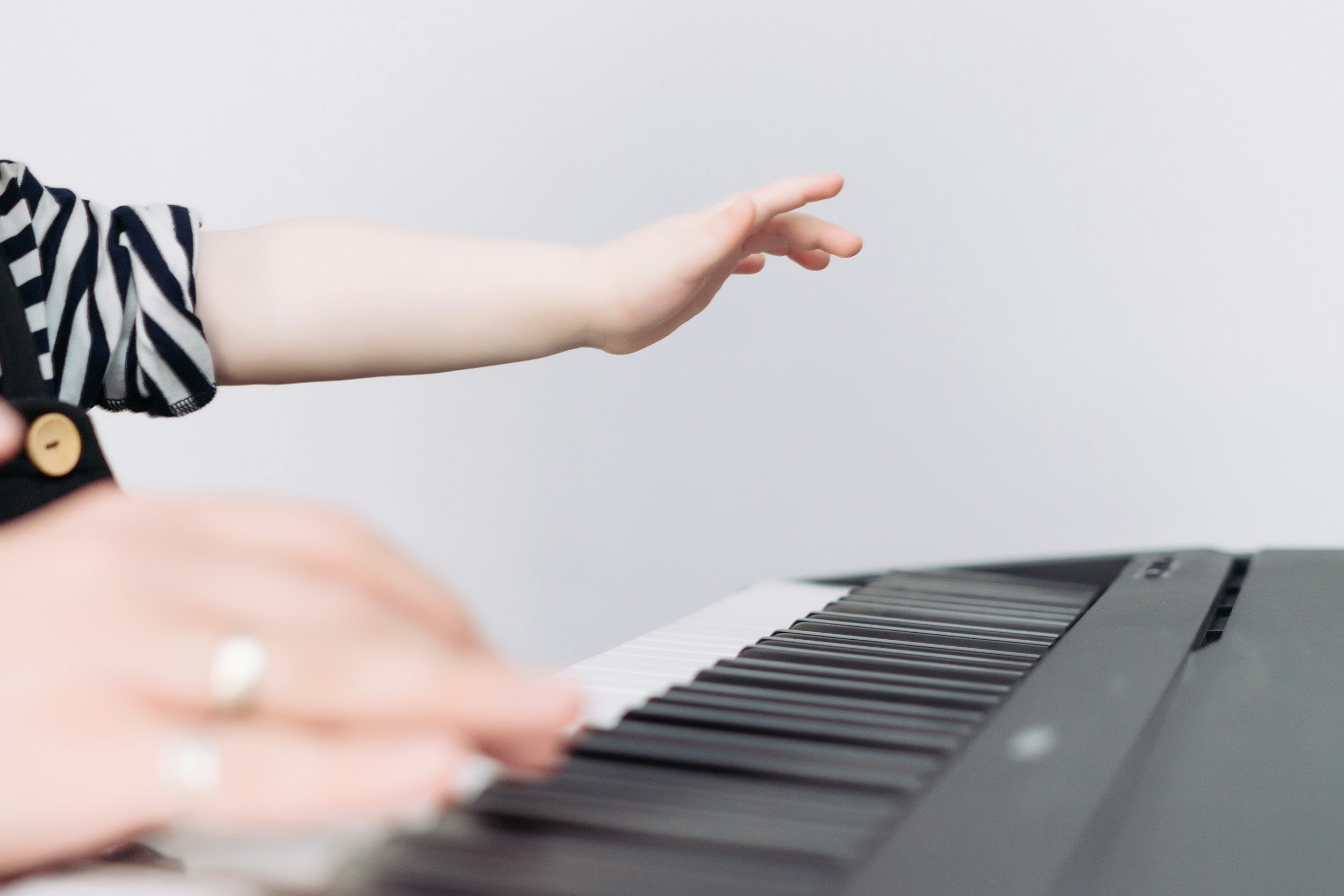 Close-up of a person's hand playing a digital piano, with a focus on the fingers and part of the hand, against a plain gray background.
