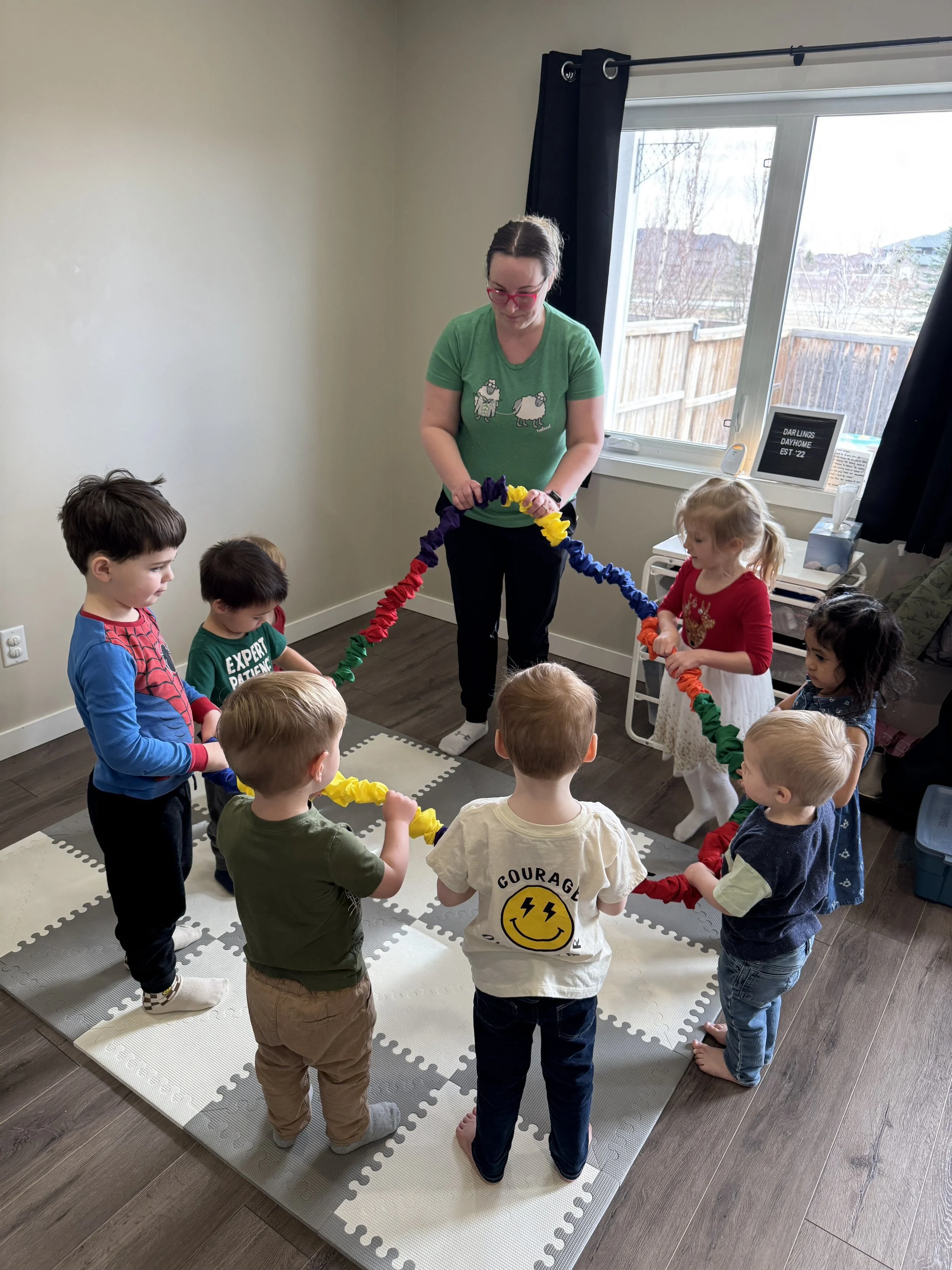 Children and Meagan Pon standing in a circle, holding a colorful paper chain in a room with a window and a sign
