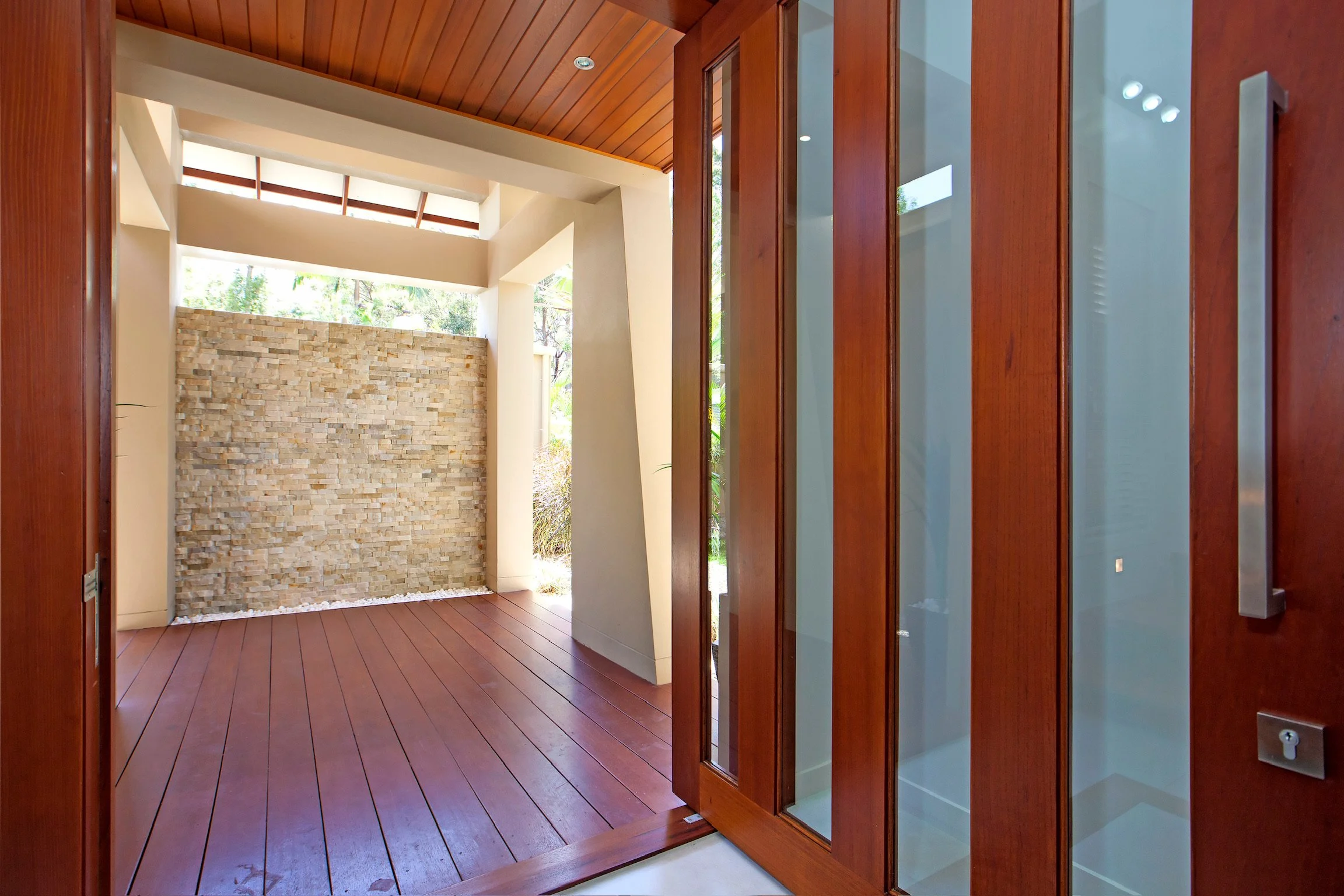 Interior view of a modern house with wooden floors, a stone accent wall, and large windows or glass doors.
