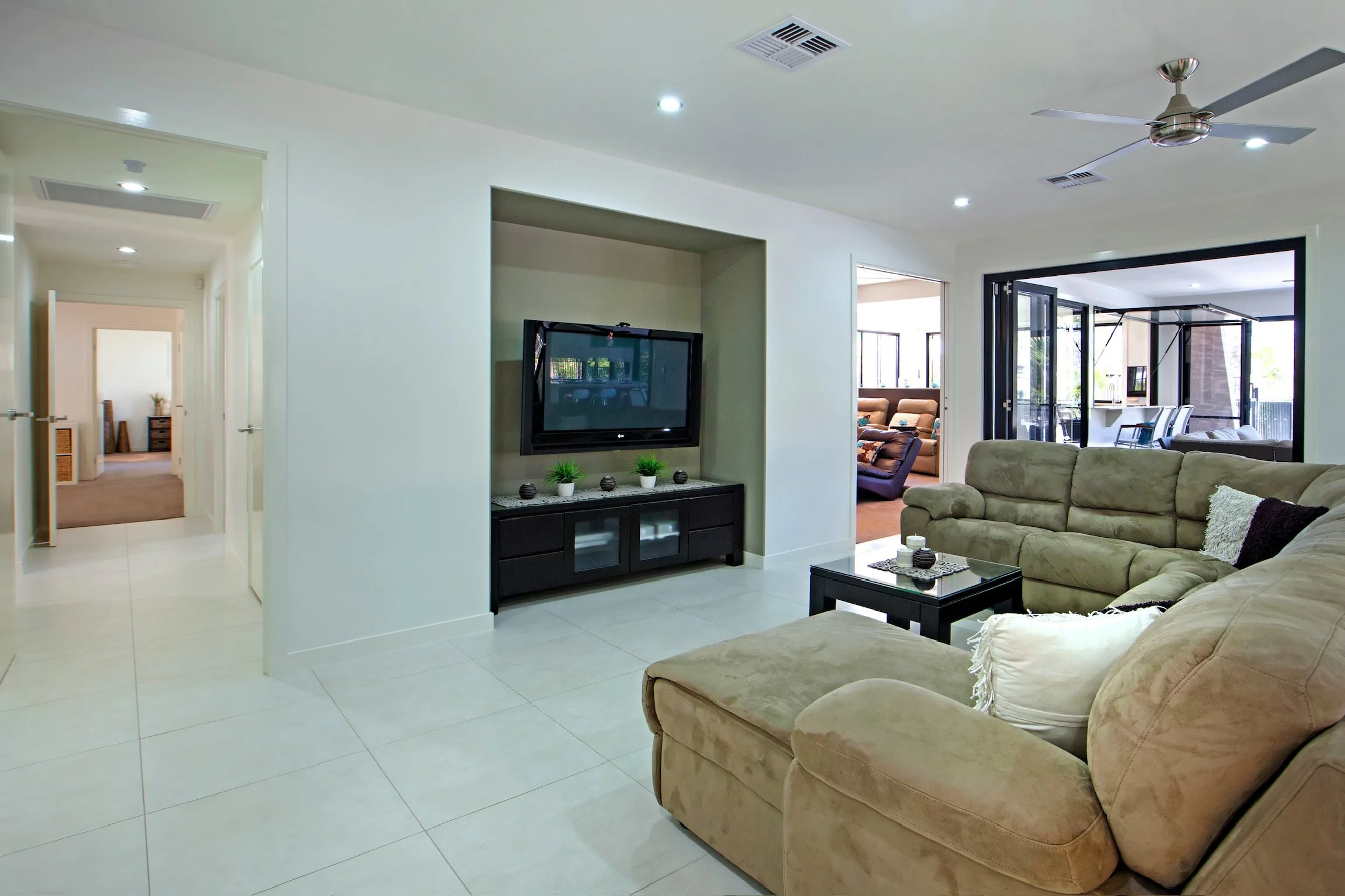 Living room with beige sofa set, black coffee table, TV on a stand, and open sliding glass doors leading to outdoor patio.