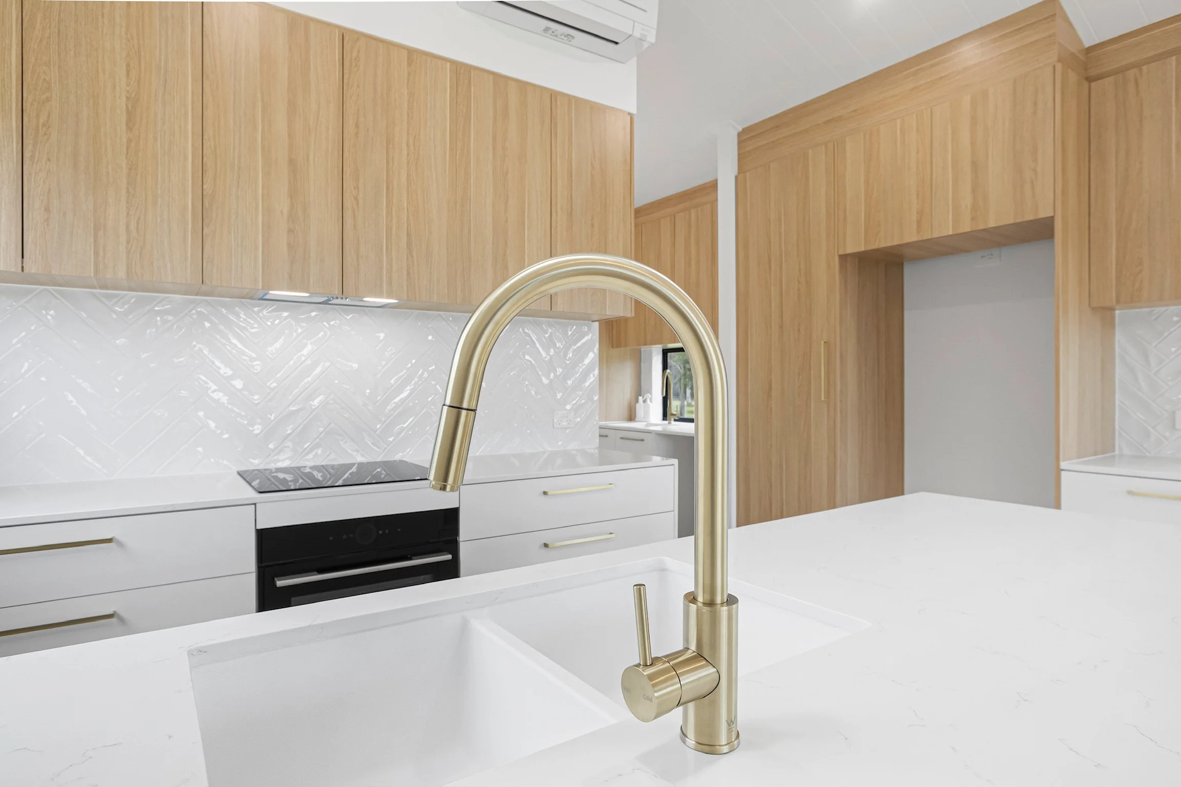 Modern kitchen with wooden cabinets, white countertops, a gold faucet, and a white subway tile backsplash.