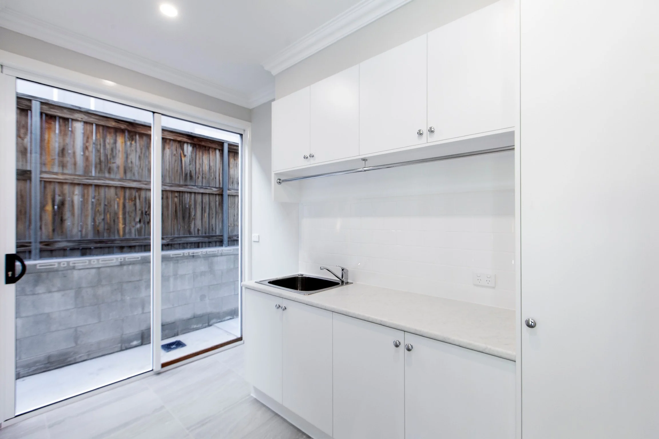 Modern kitchen with white cabinets, a black sink, and a sliding glass door leading outside to a wooden fence.