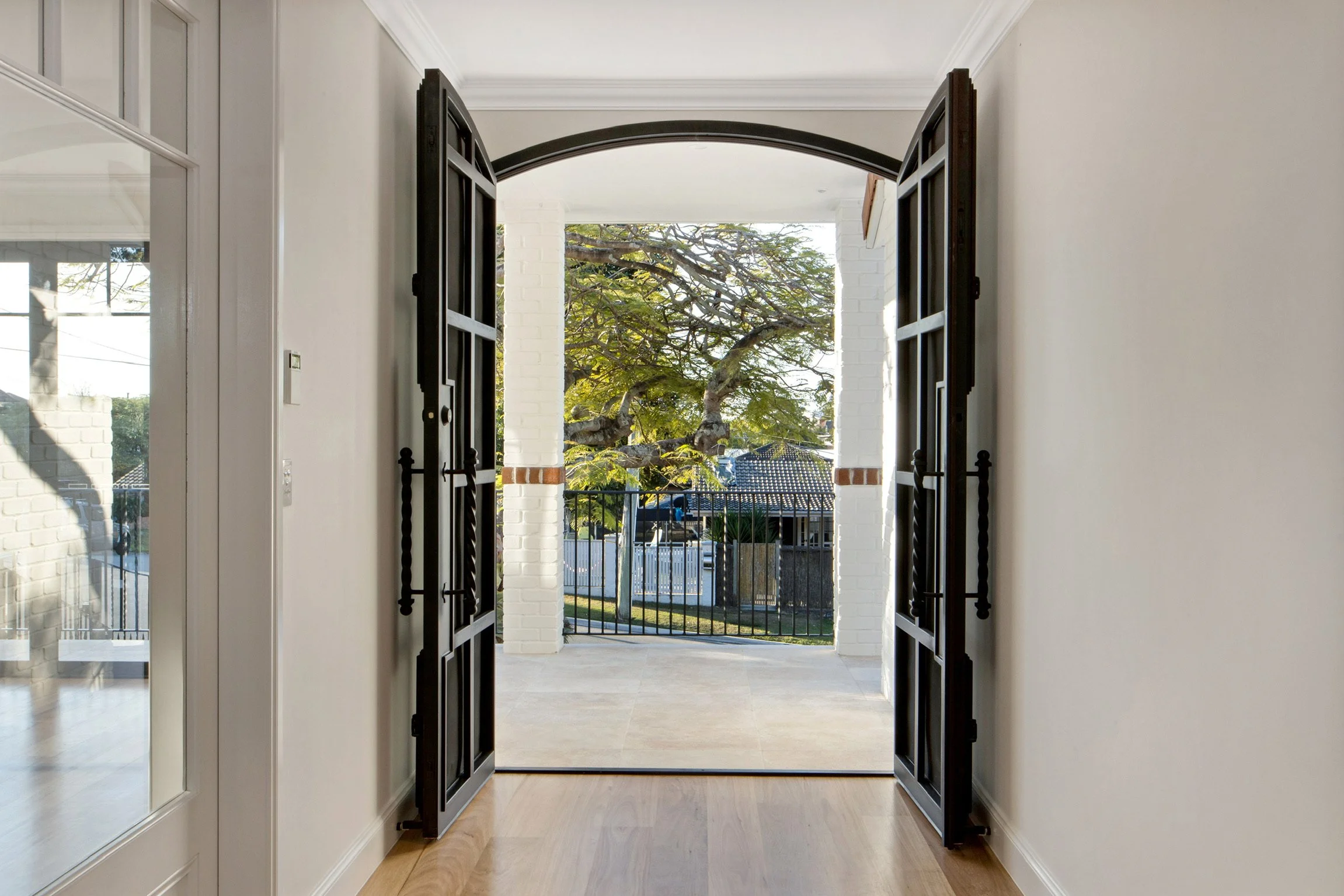 Open double black doors leading to a porch with a view of trees and neighboring houses.