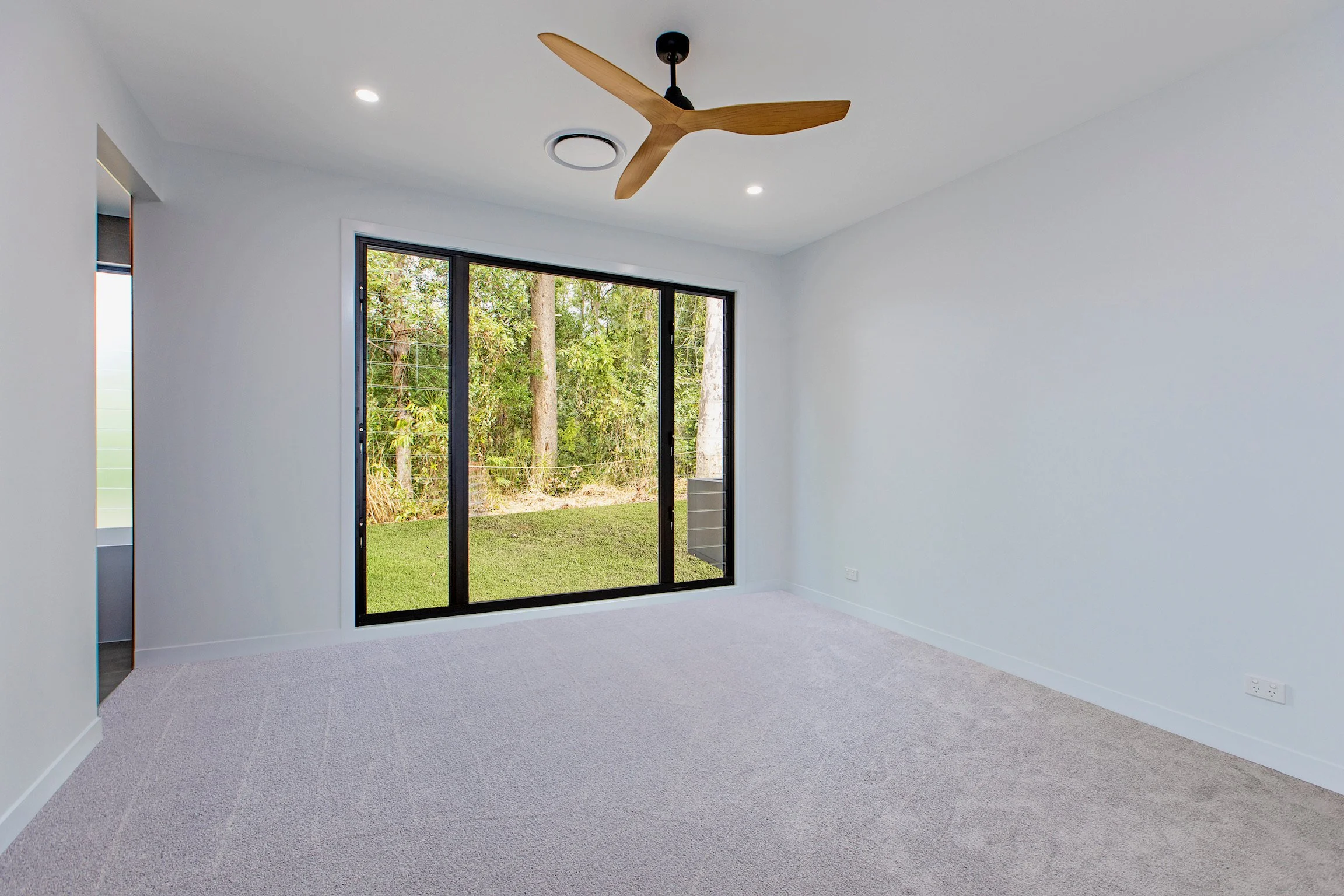 Empty room with beige carpet, white walls, and a large sliding glass door leading to a green outdoor area with trees.