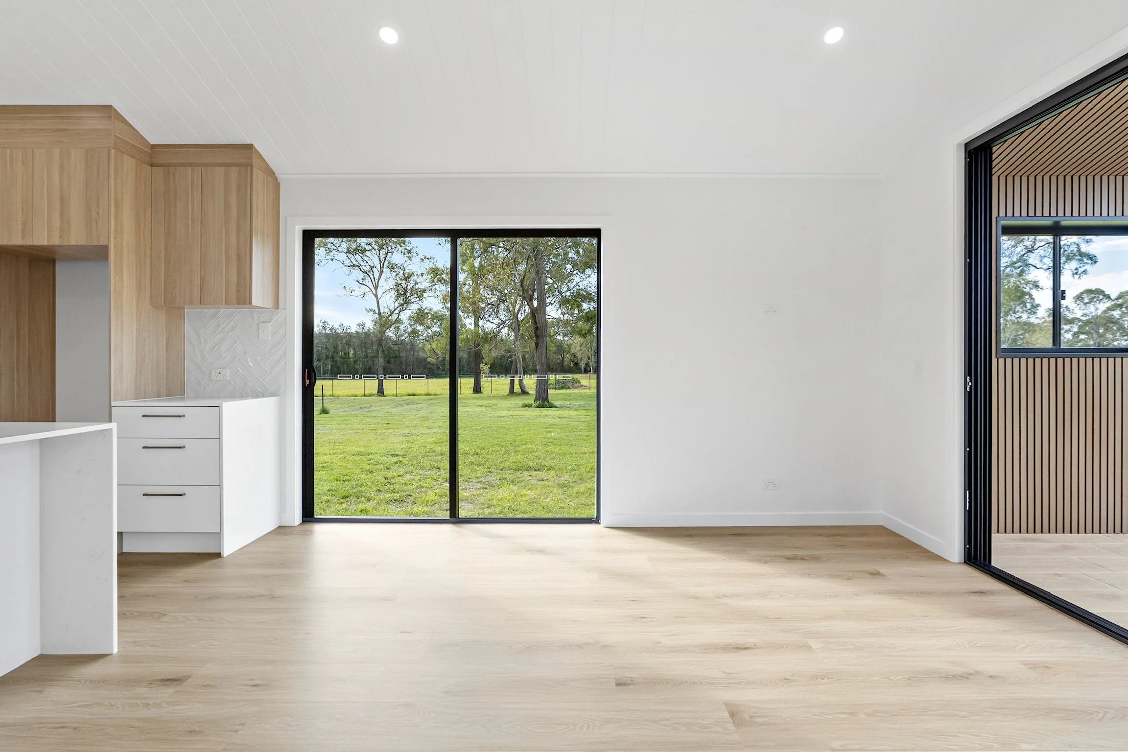Empty modern living room with large sliding glass doors showing a green outdoor landscape with trees