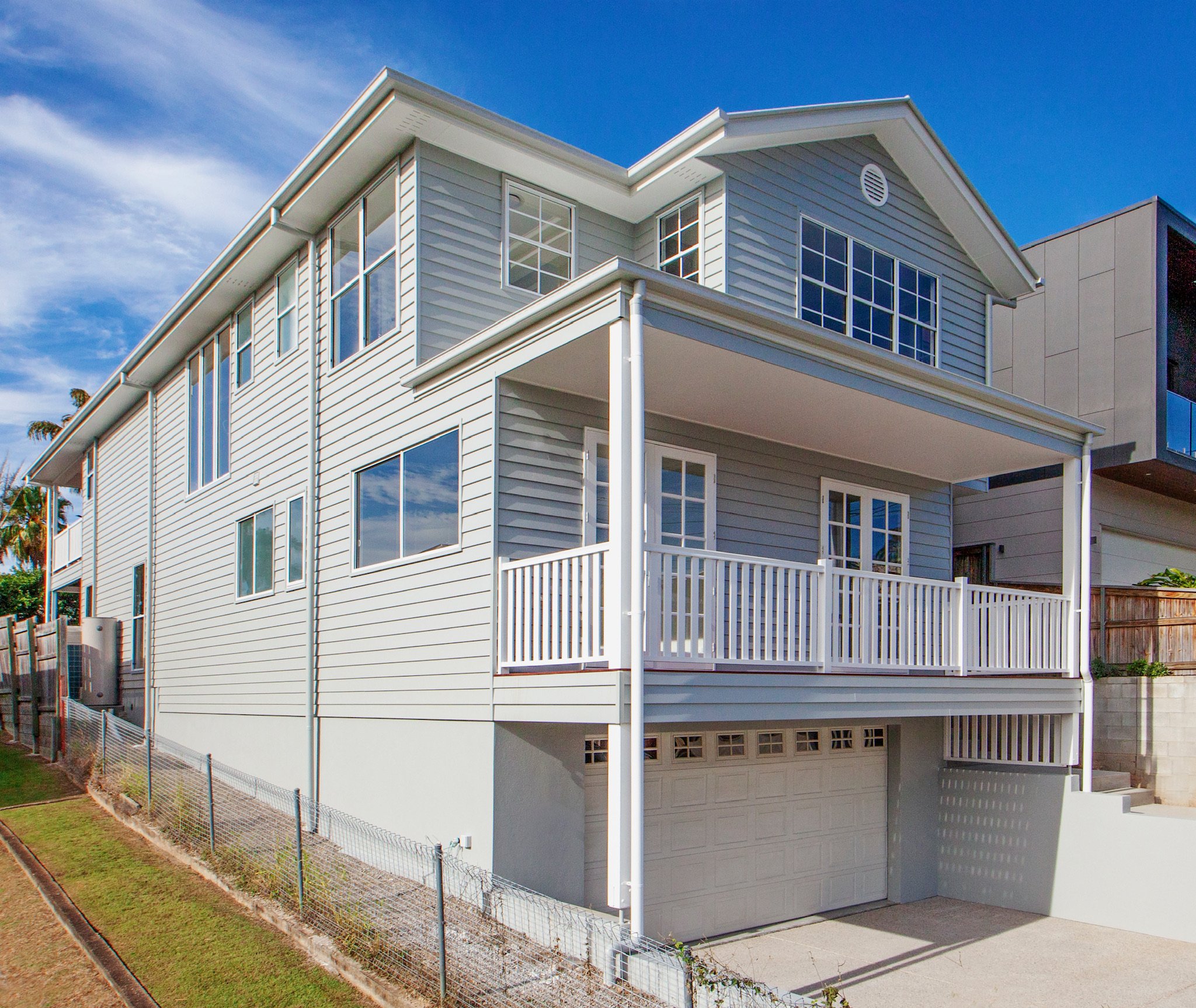 A modern, white multi-story house with multiple large windows and a small balcony under a blue sky with some clouds.