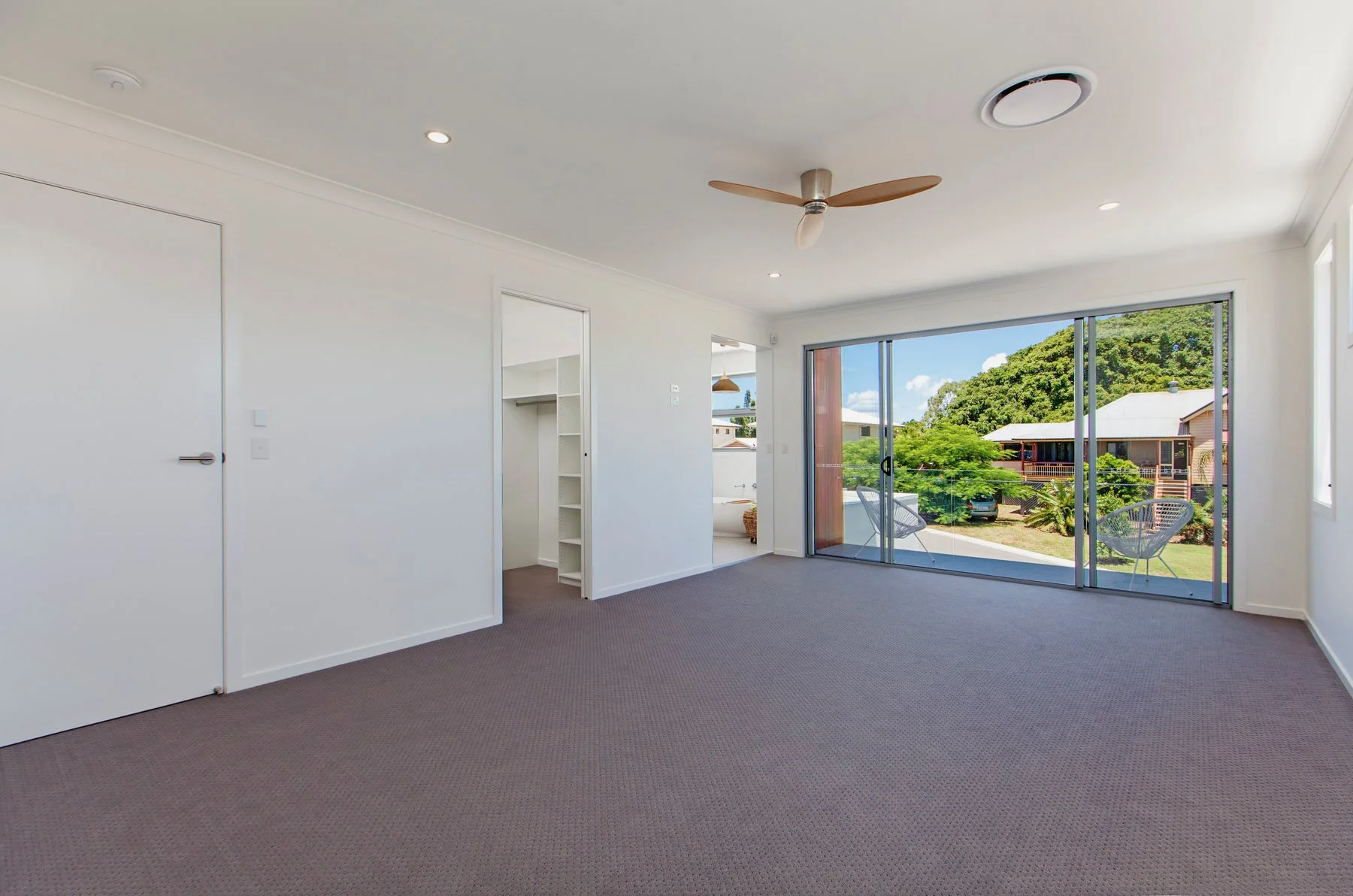 Empty living room with sliding glass door leading to outdoor patio, ceiling fan, white walls, and carpeted floor.