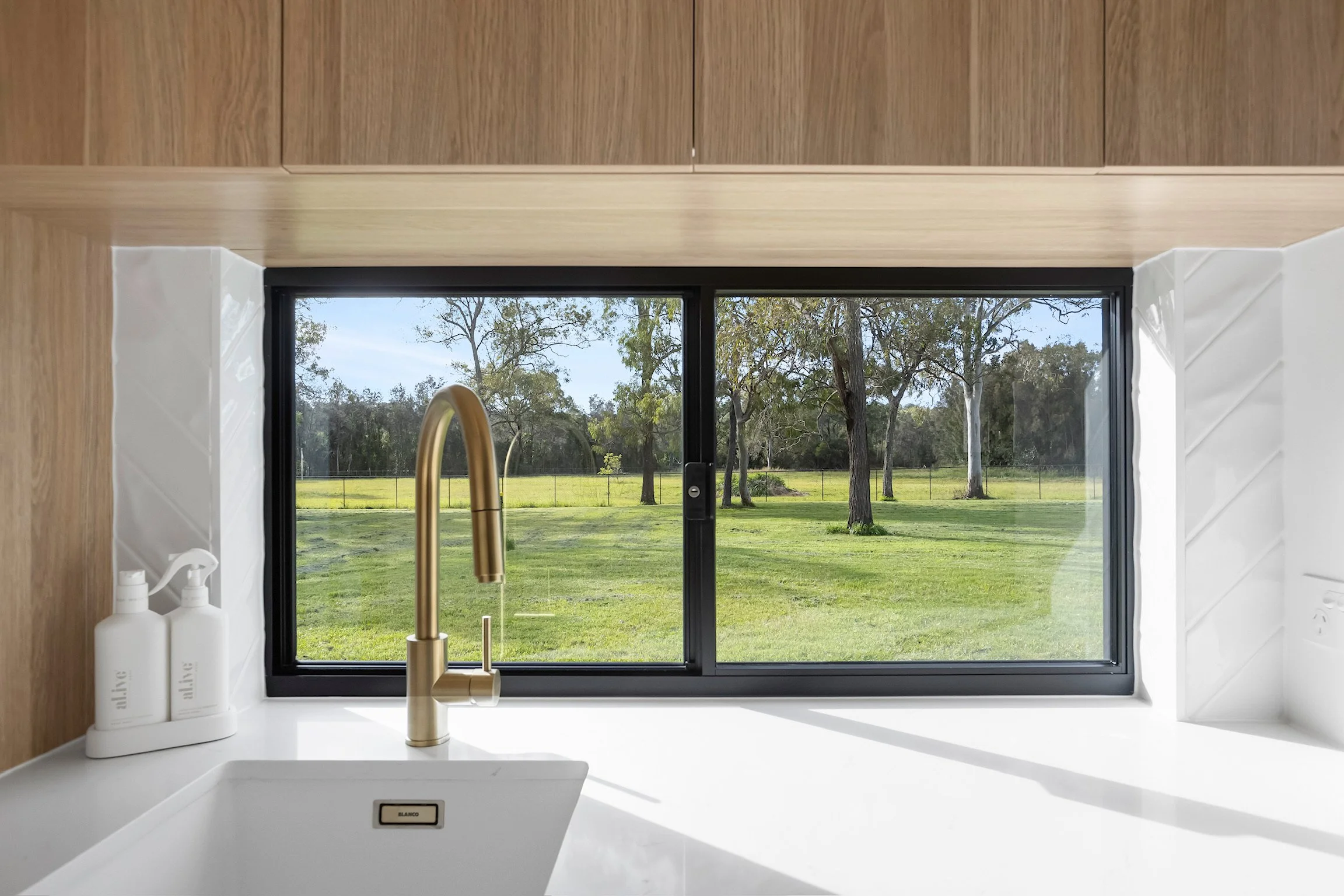 View from a kitchen window showing trees and a grassy field outside.