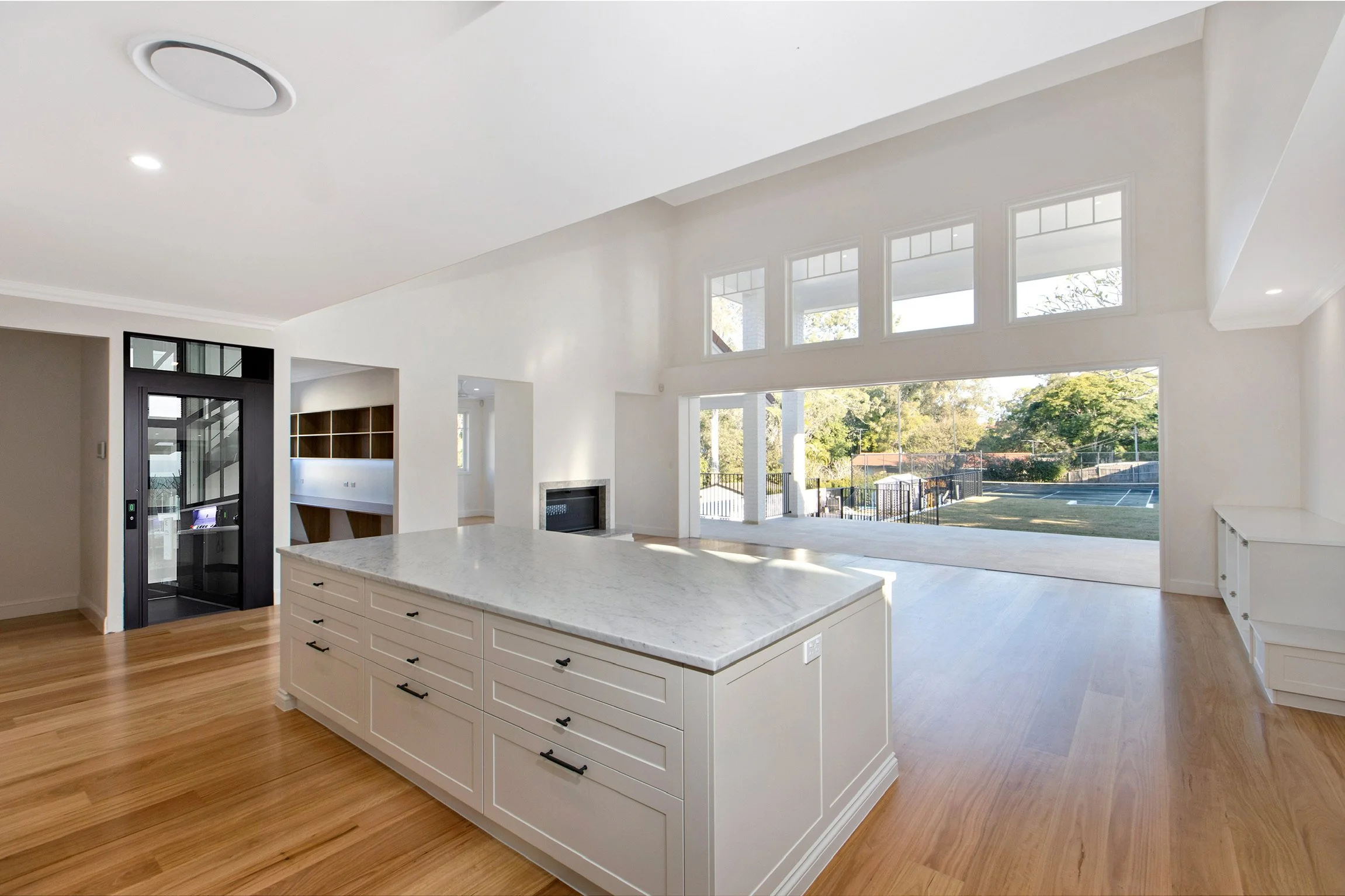 Open living space with large windows, white walls, and hardwood floors, featuring a kitchen island with a marble countertop.
