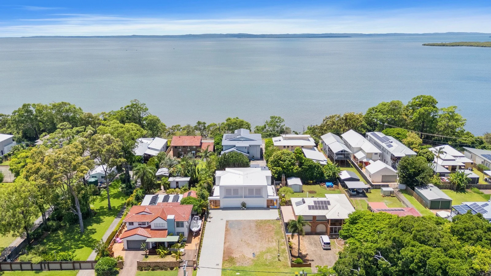 Aerial view of a residential neighborhood near a large body of water with trees and houses, some with solar panels.