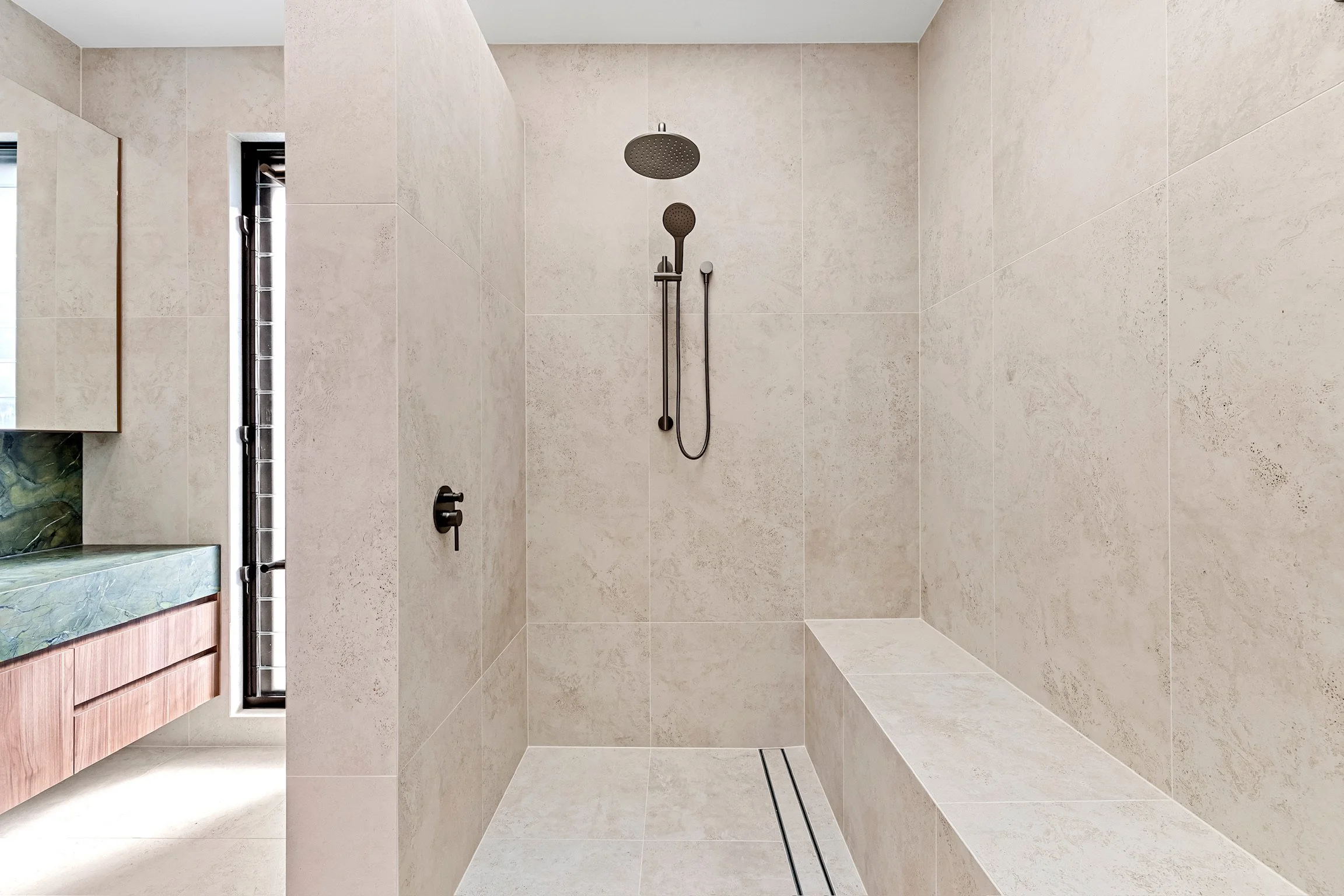 Modern walk-in shower with beige tiles, a rainfall showerhead, a handheld showerhead, and a small bench.